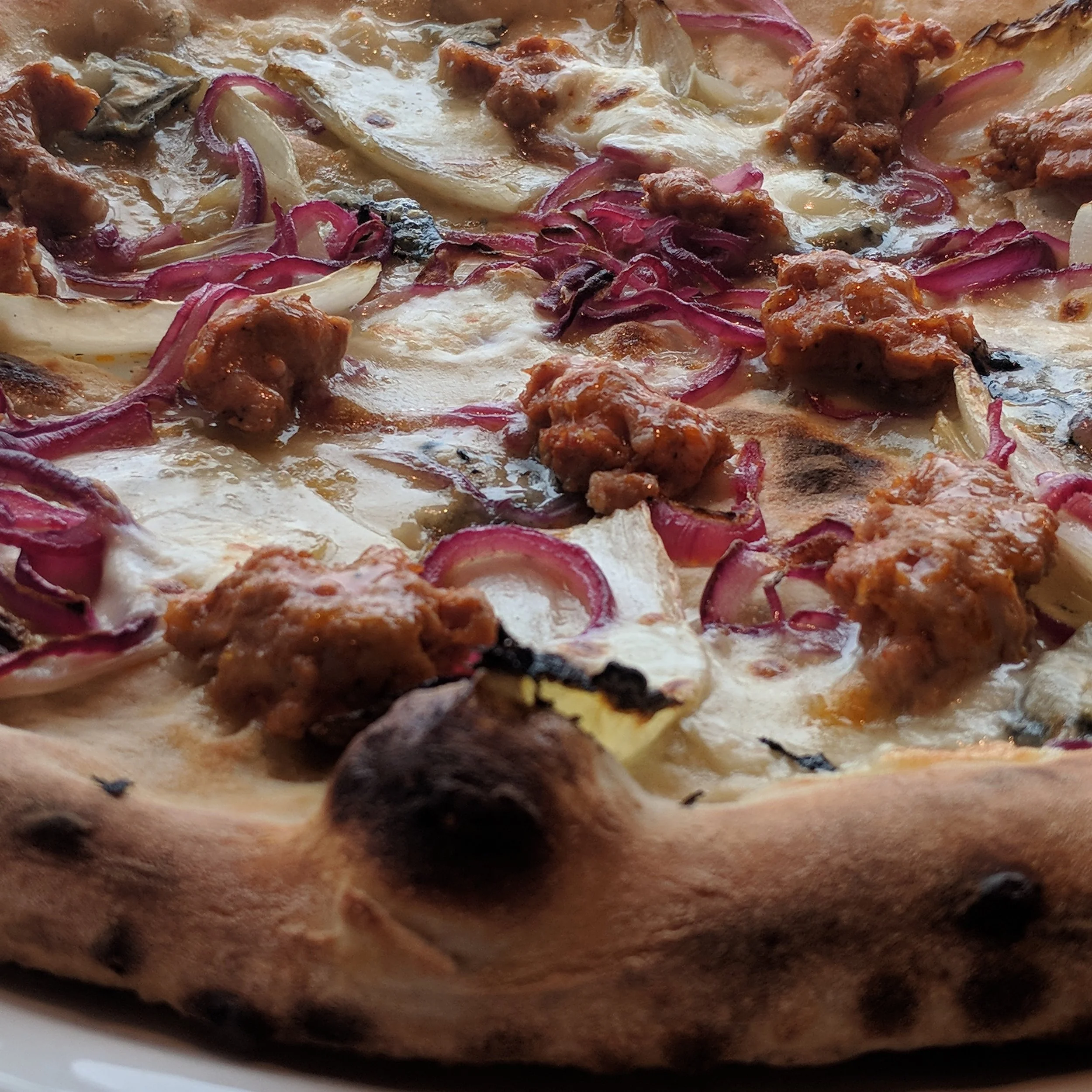 Close-up of a pizza with cheese, red onions, beef, and a wood-fired crust.