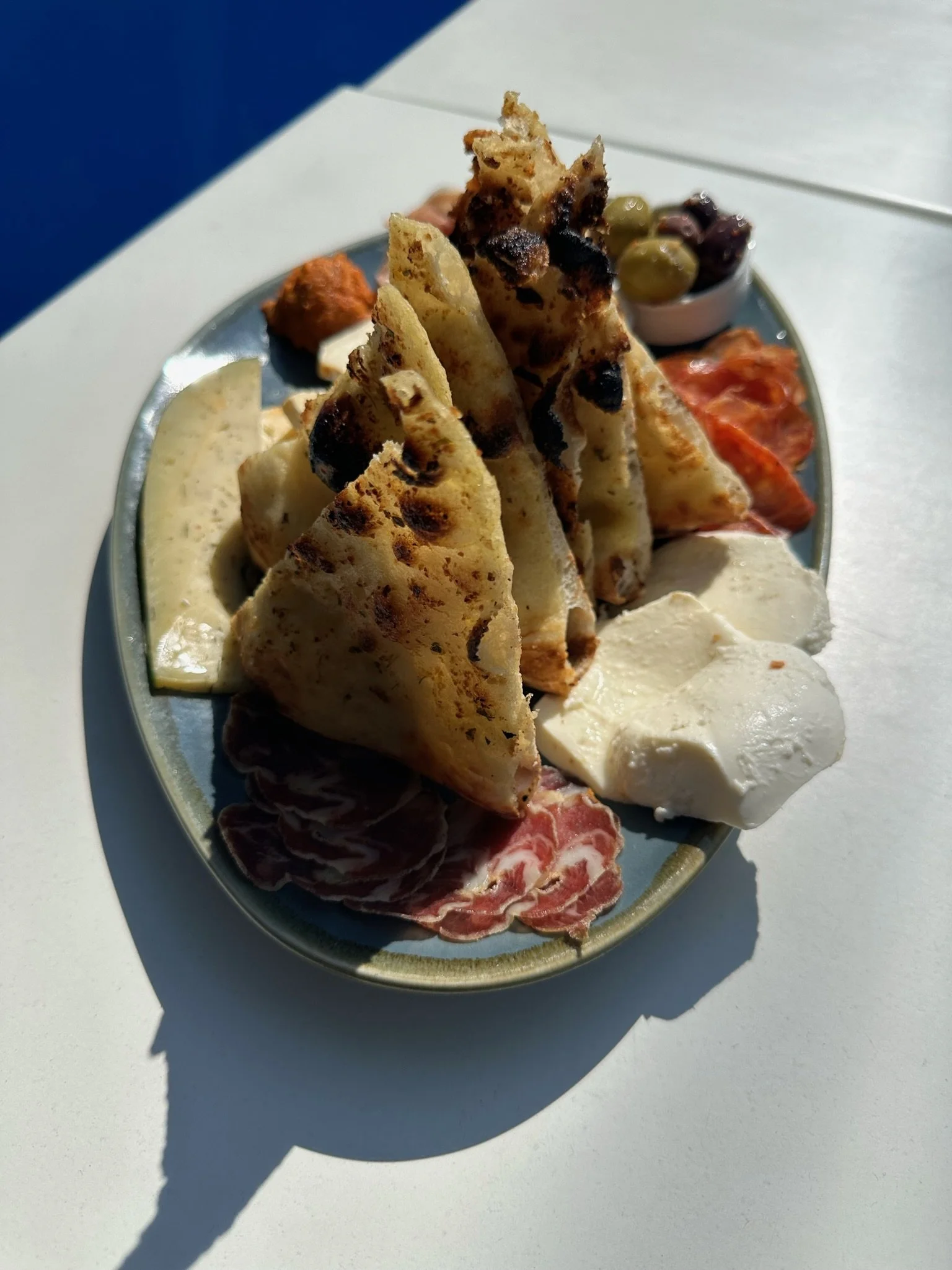 Plate with flatbread, cheese, sliced meat, olives, and vegetables