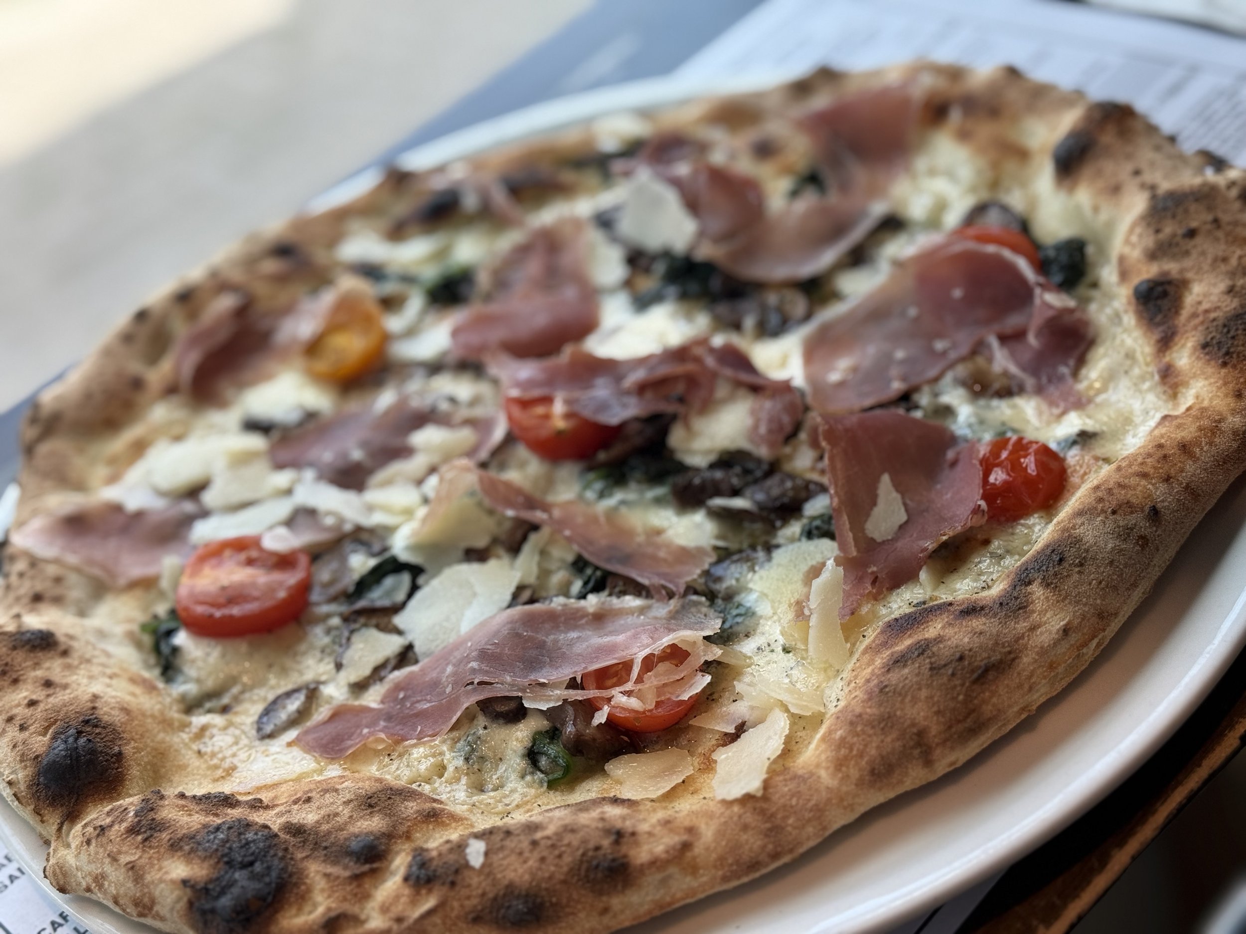 Close-up of a pizza with cherry tomatoes, prosciutto, cheese, and greens on a toasted crust.