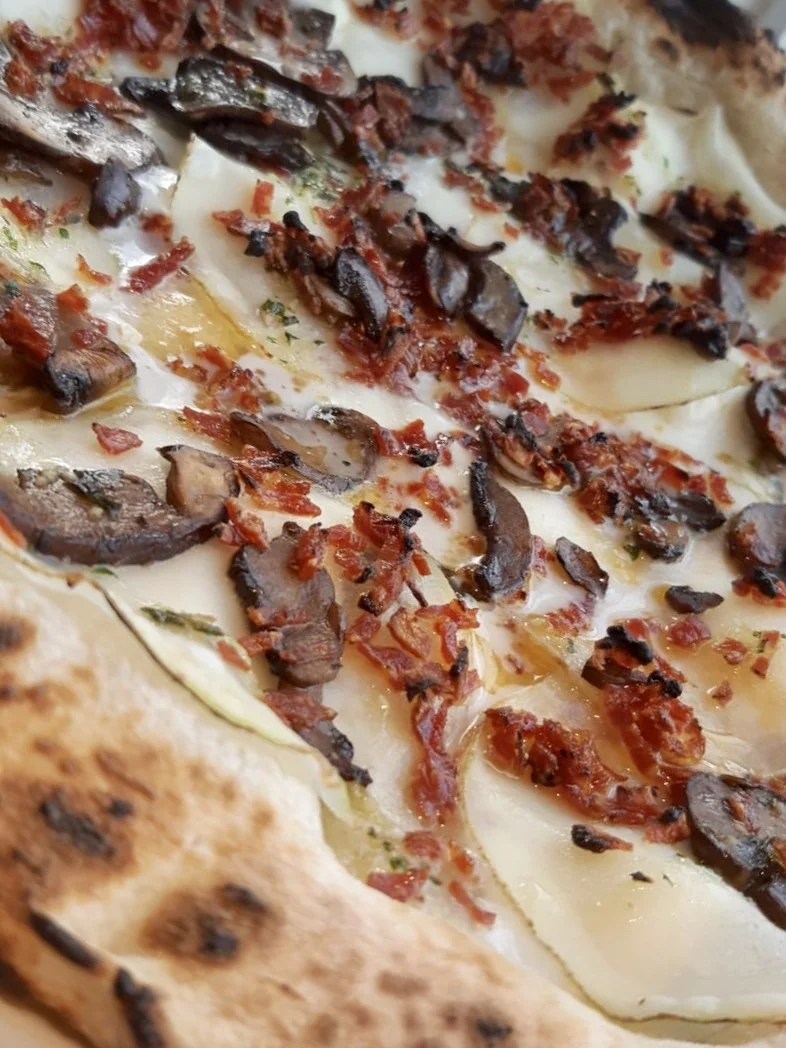 Close-up of a pizza with mushrooms, bacon bits, melted cheese, and a bubbly, slightly charred crust.