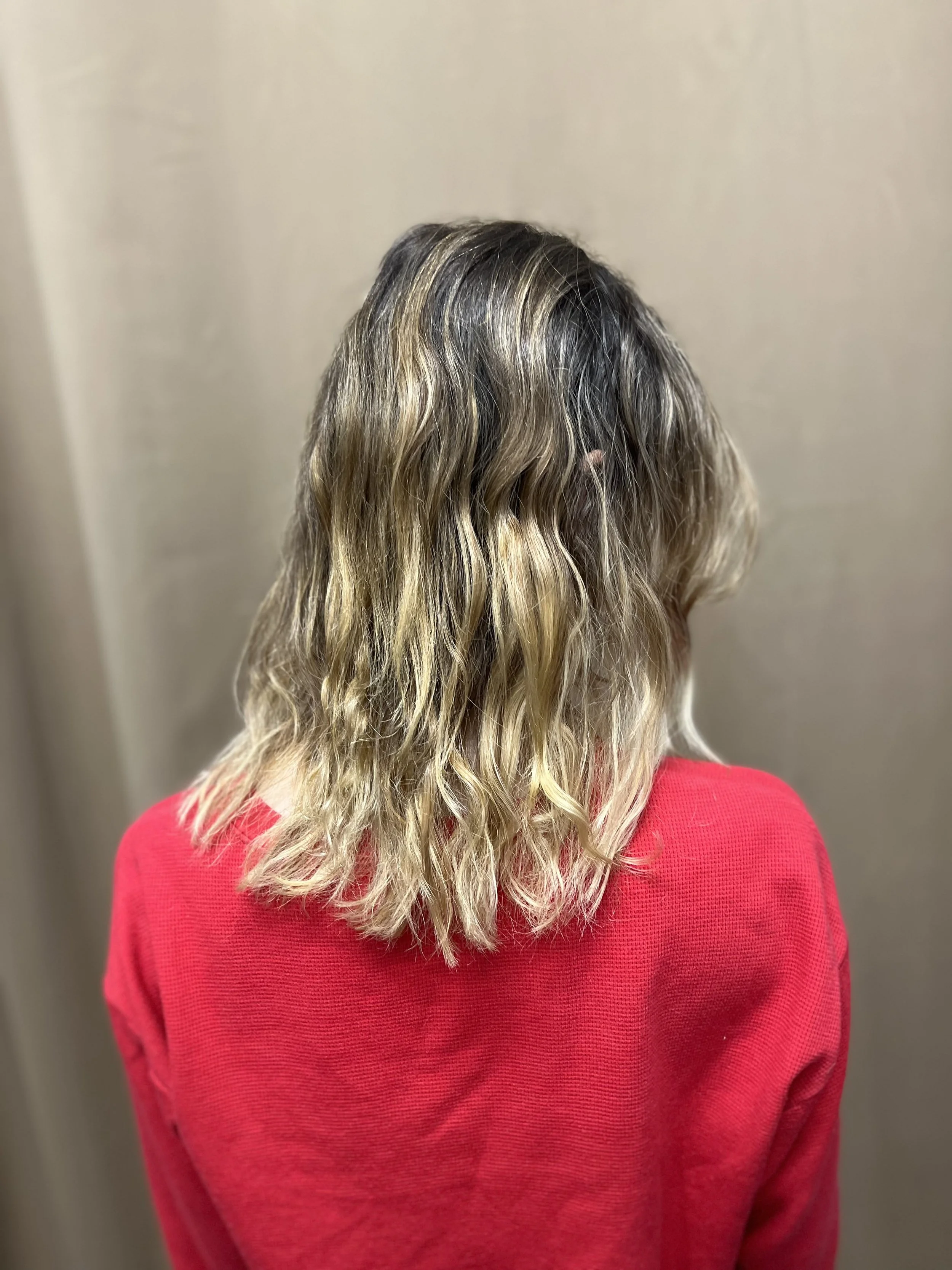 Back view of a person with wavy, blonde the hair, wearing a red sweater.