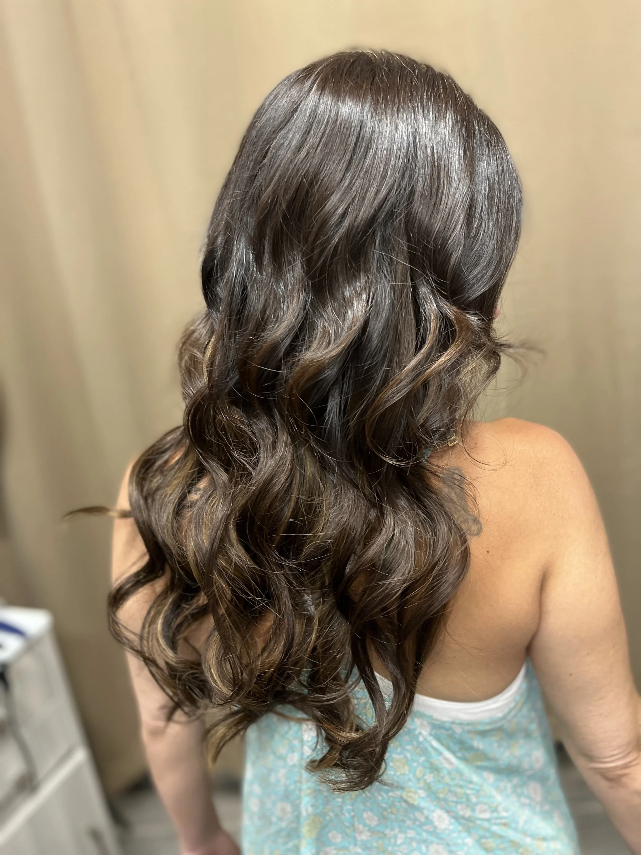 A woman with long, wavy brown hair wearing a teal floral dress, facing away from the camera.