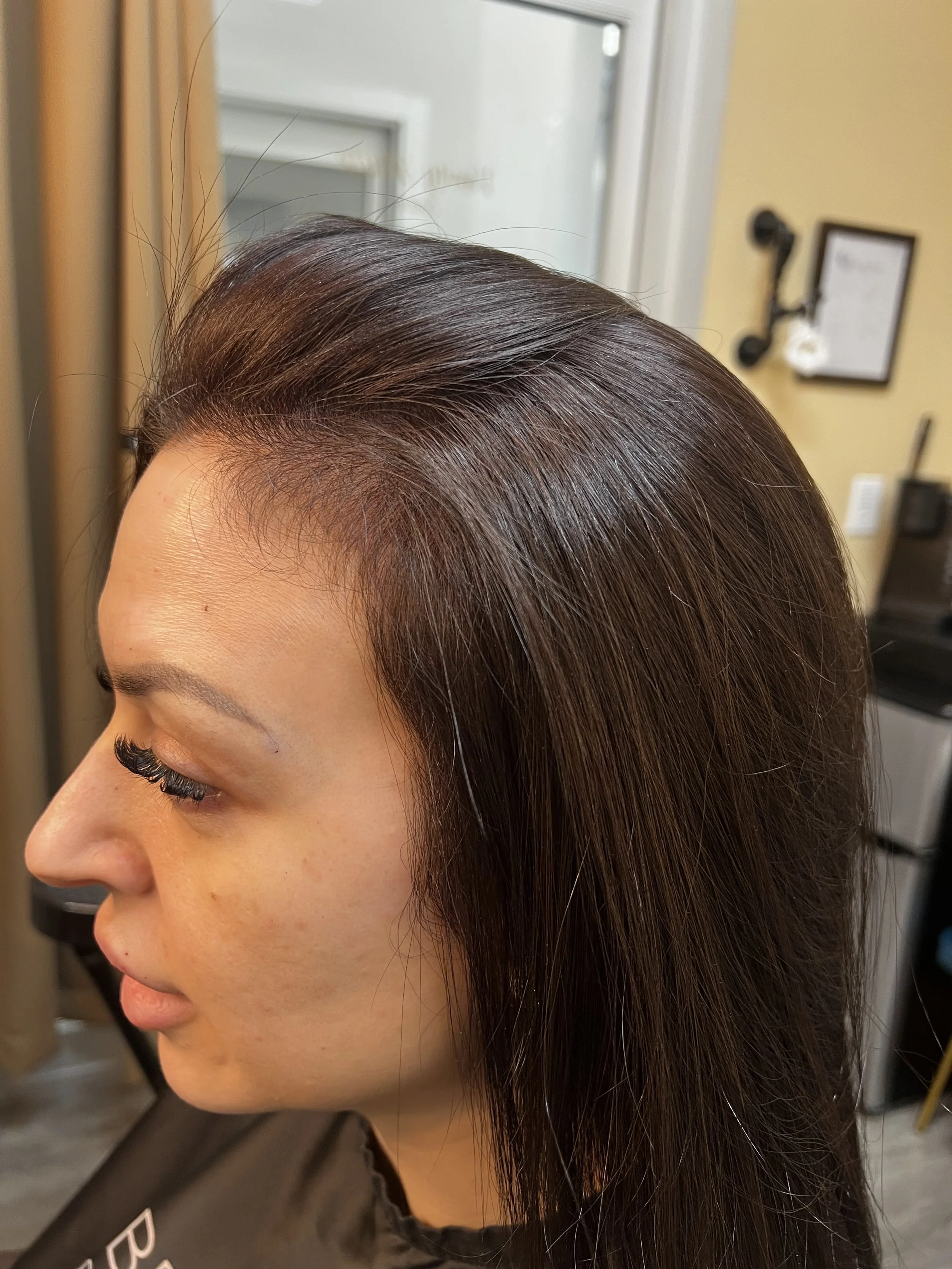 Close-up of a woman's side profile with smooth, shiny, dark brown hair in a salon setting.