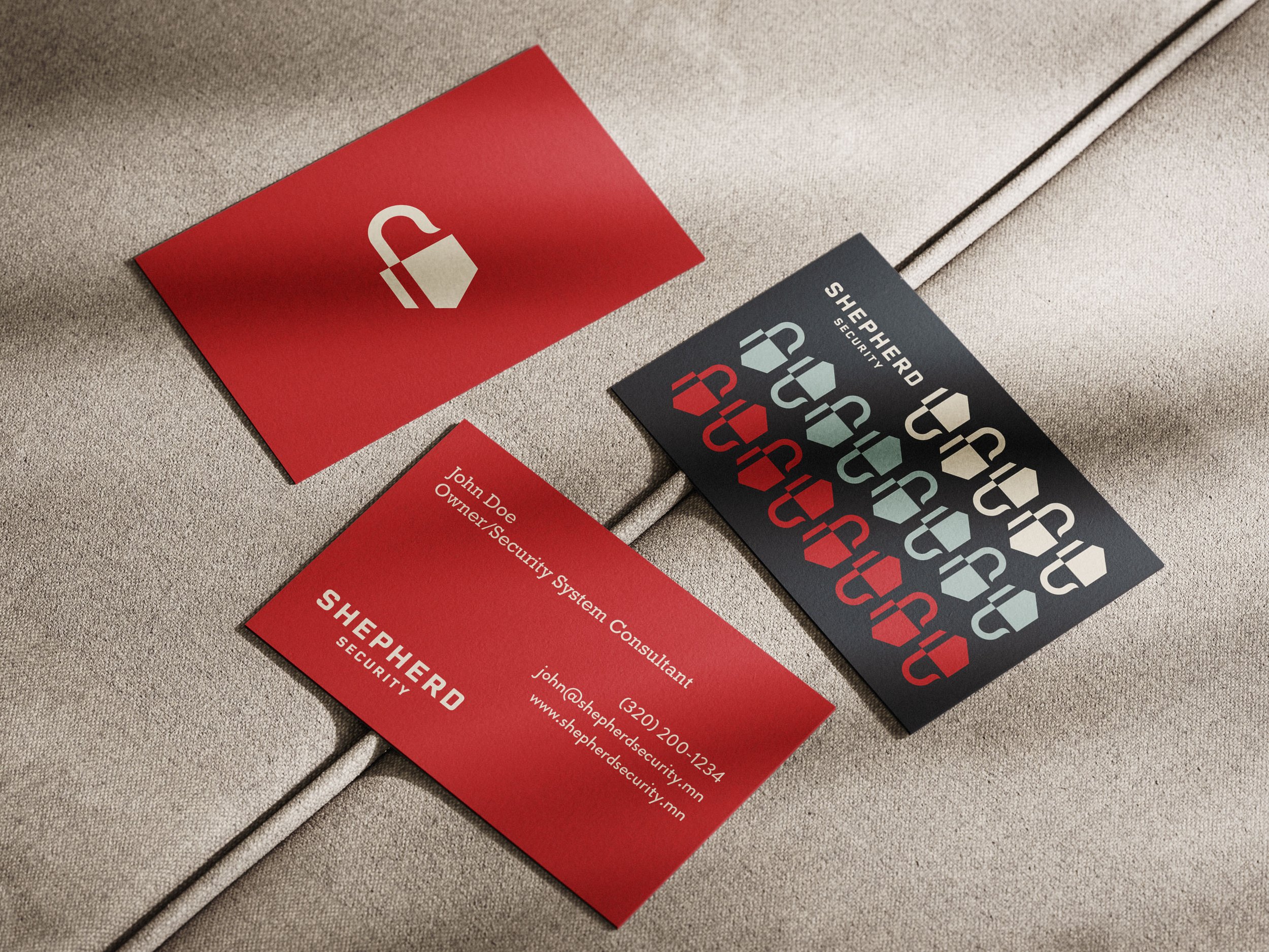Business cards and a sticker with a shield logo and the words 'Shepherd Security' on a fabric surface.