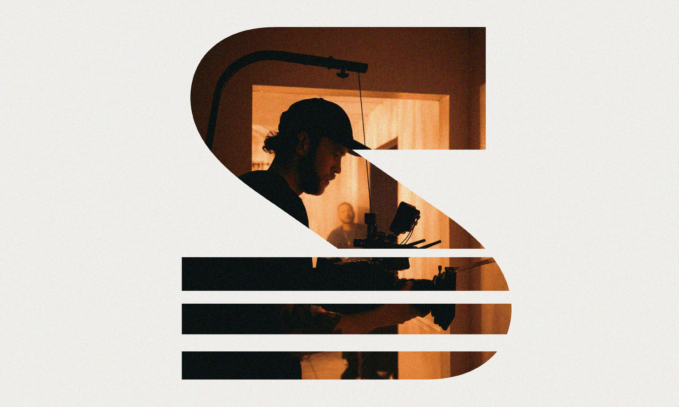 Silhouette of a man working with camera and filming equipment inside a house, with a person blurred in the background, viewed through a sliced Starbucks logo.