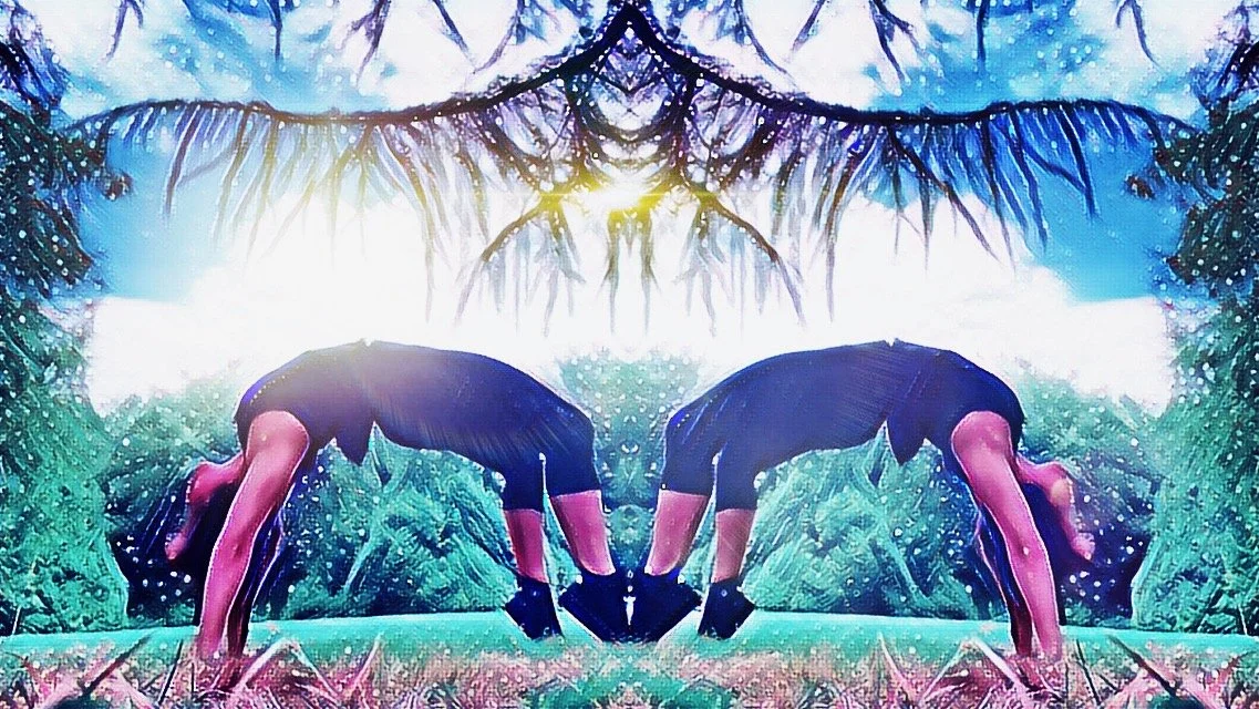 Two women in black dresses and gloves perform a synchronized yoga pose with their hands touching, outdoors in a green park with trees and a bright sun overhead.