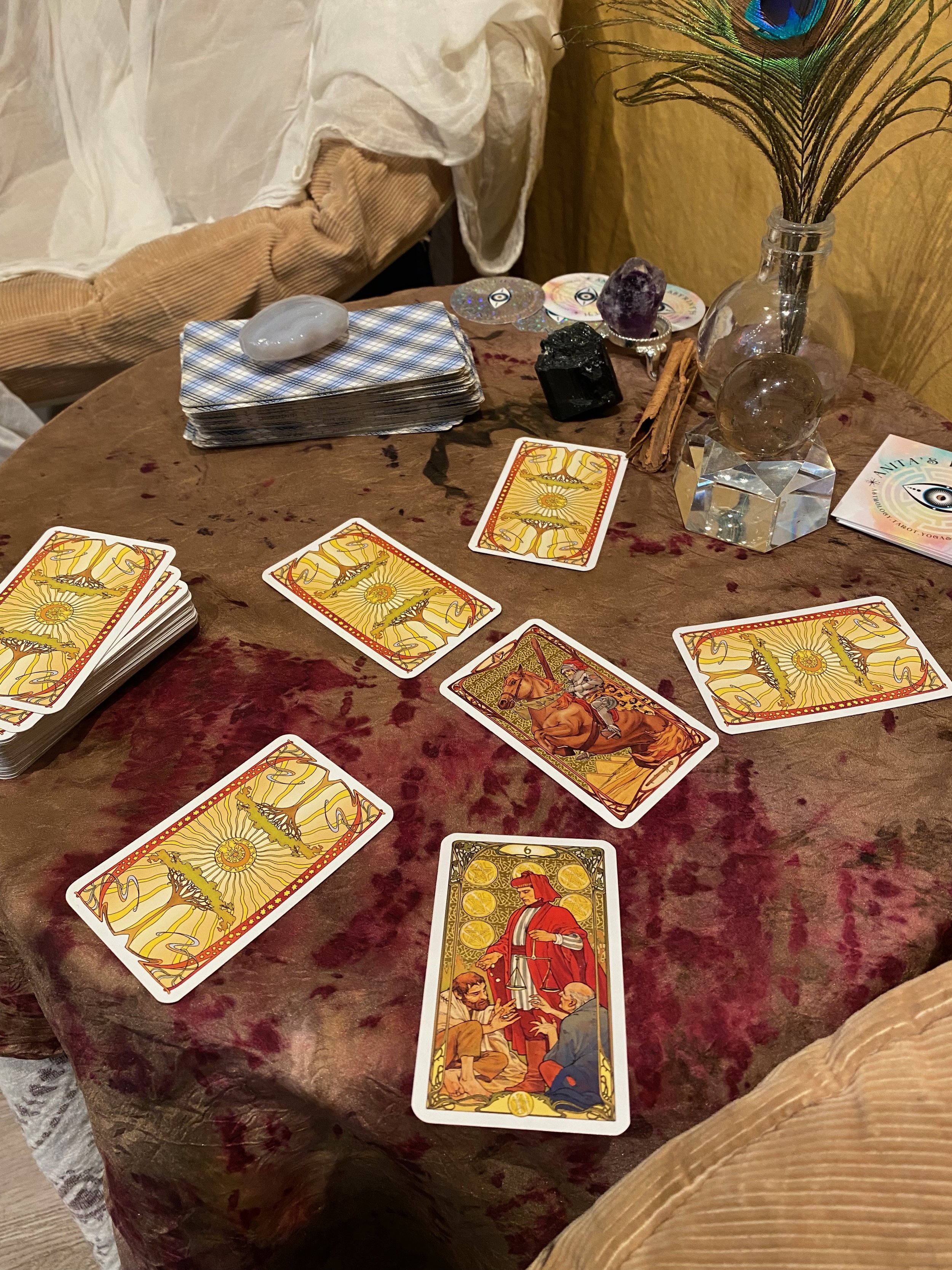 A tarot card reading setup with tarot cards spread on a red velvet tablecloth, crystals, a vase with peacock feathers, and other mystical items.