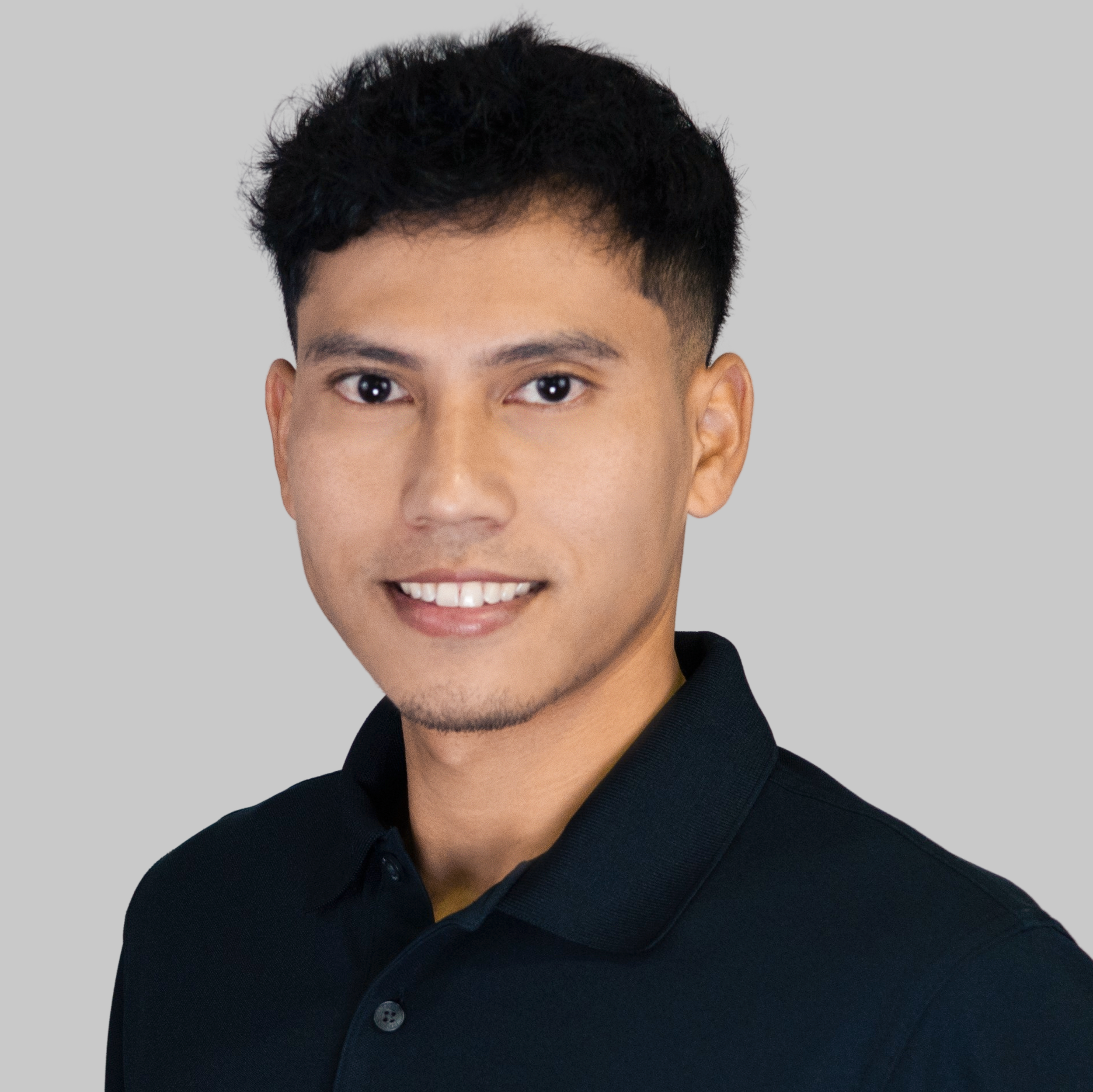 Portrait of a young man with short black hair, wearing a black collared shirt, smiling against a gray background.