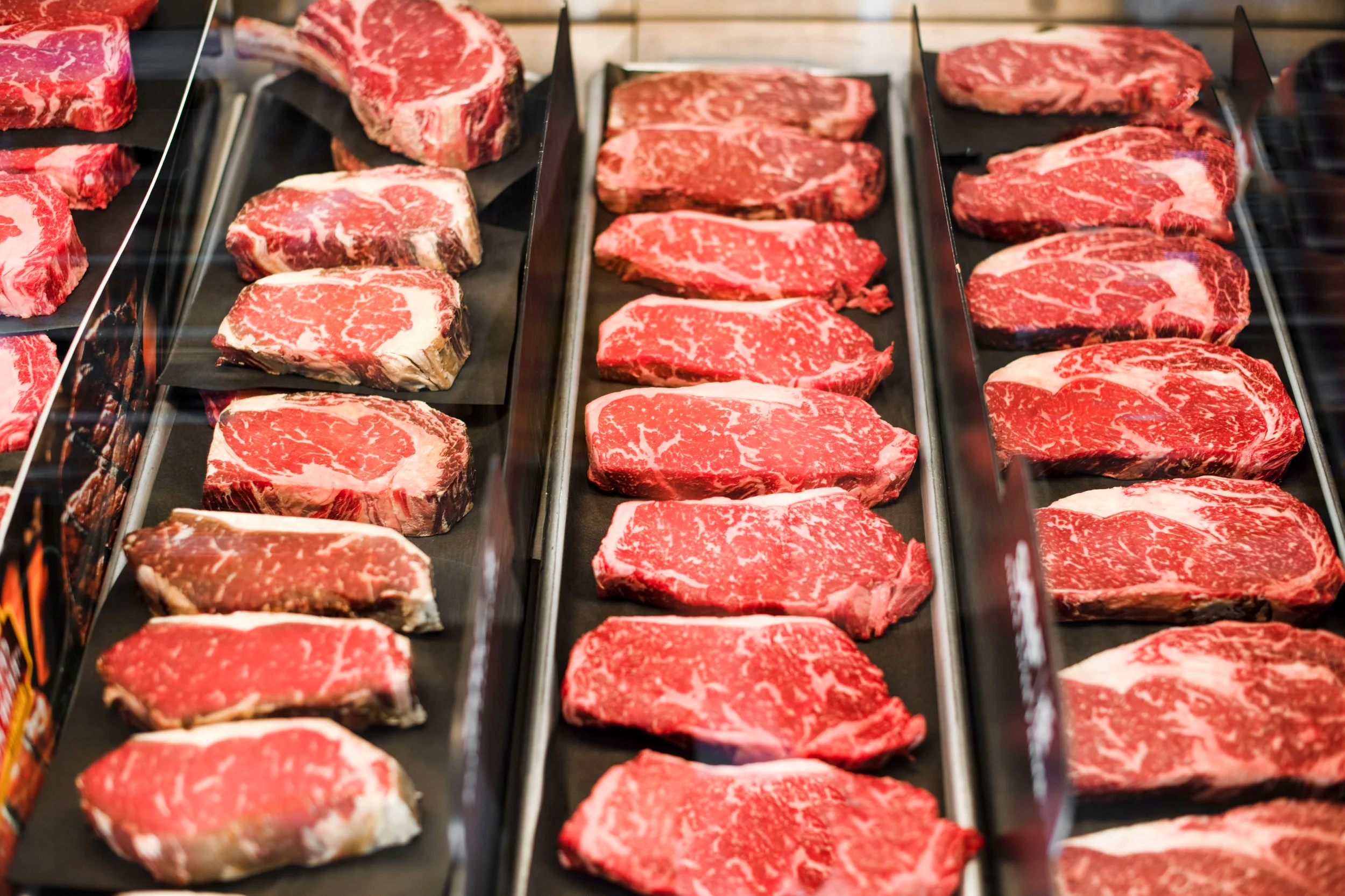 Ribeyes, New York strips,  and cuts of steak in a butcher case.