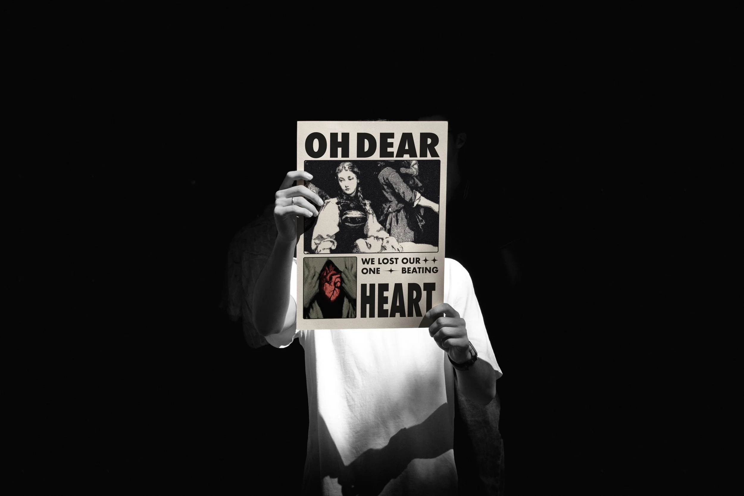 A person holding a protest sign with the words 'OH DEAR' at the top, a black-and-white photo of a woman in the center, and the text 'WE LOST OUR ONE BEATING HEART' below, against a dark background.