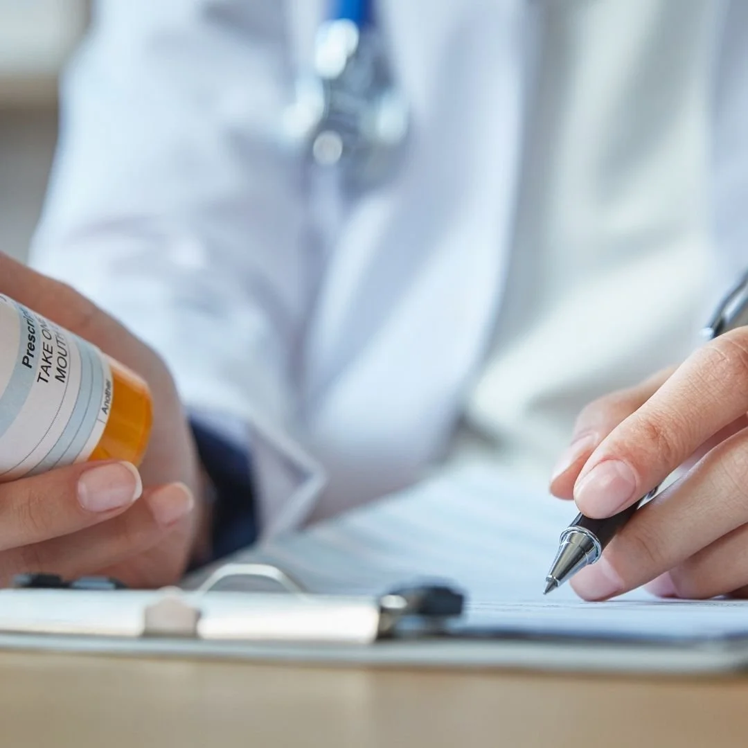 Close-up of a healthcare professional in a white coat taking notes on a clipboard with a pen, holding a prescription medication bottle in the other hand.