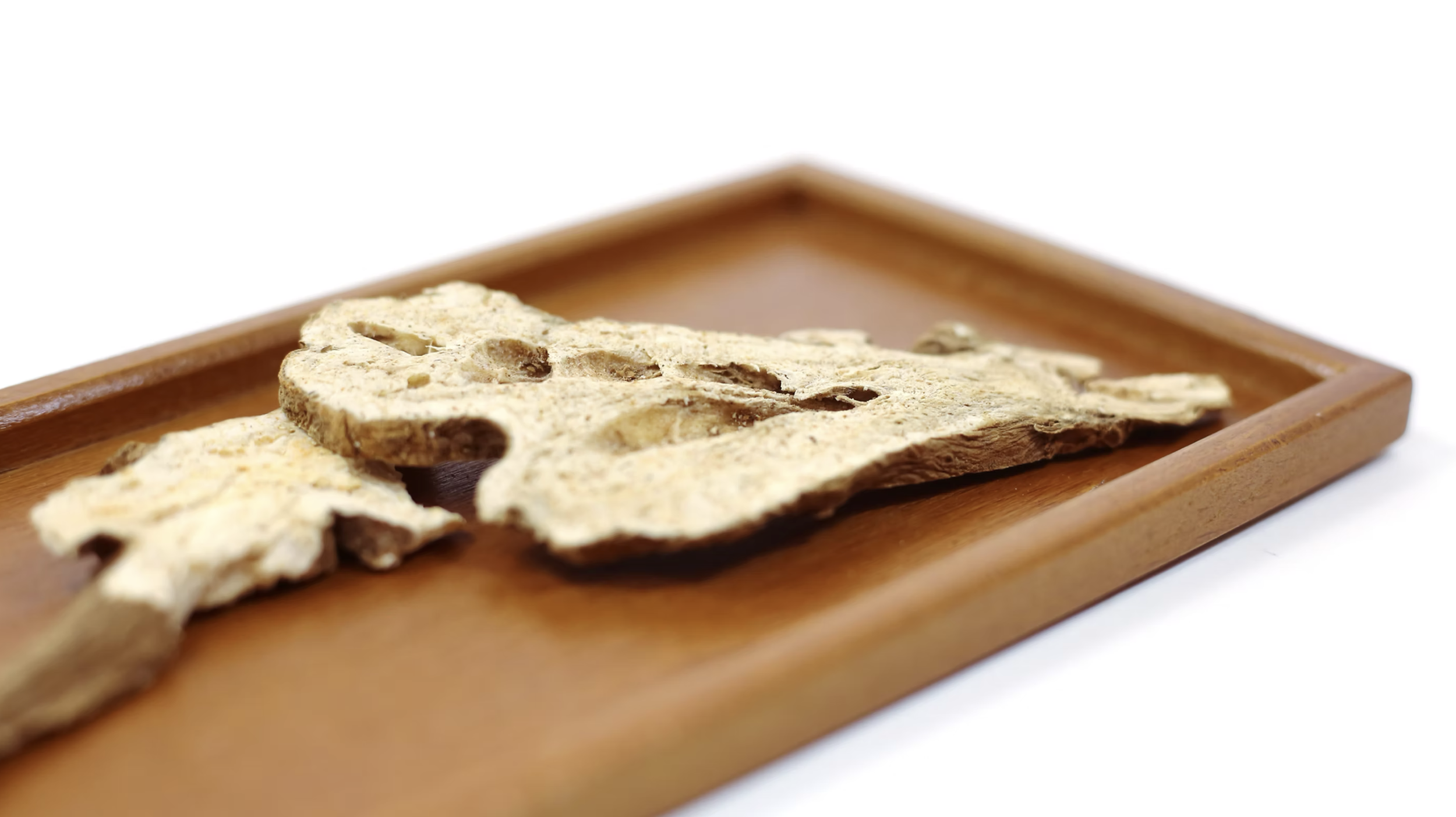 Close-up of a dried mushroom on a wooden tray against a white background.