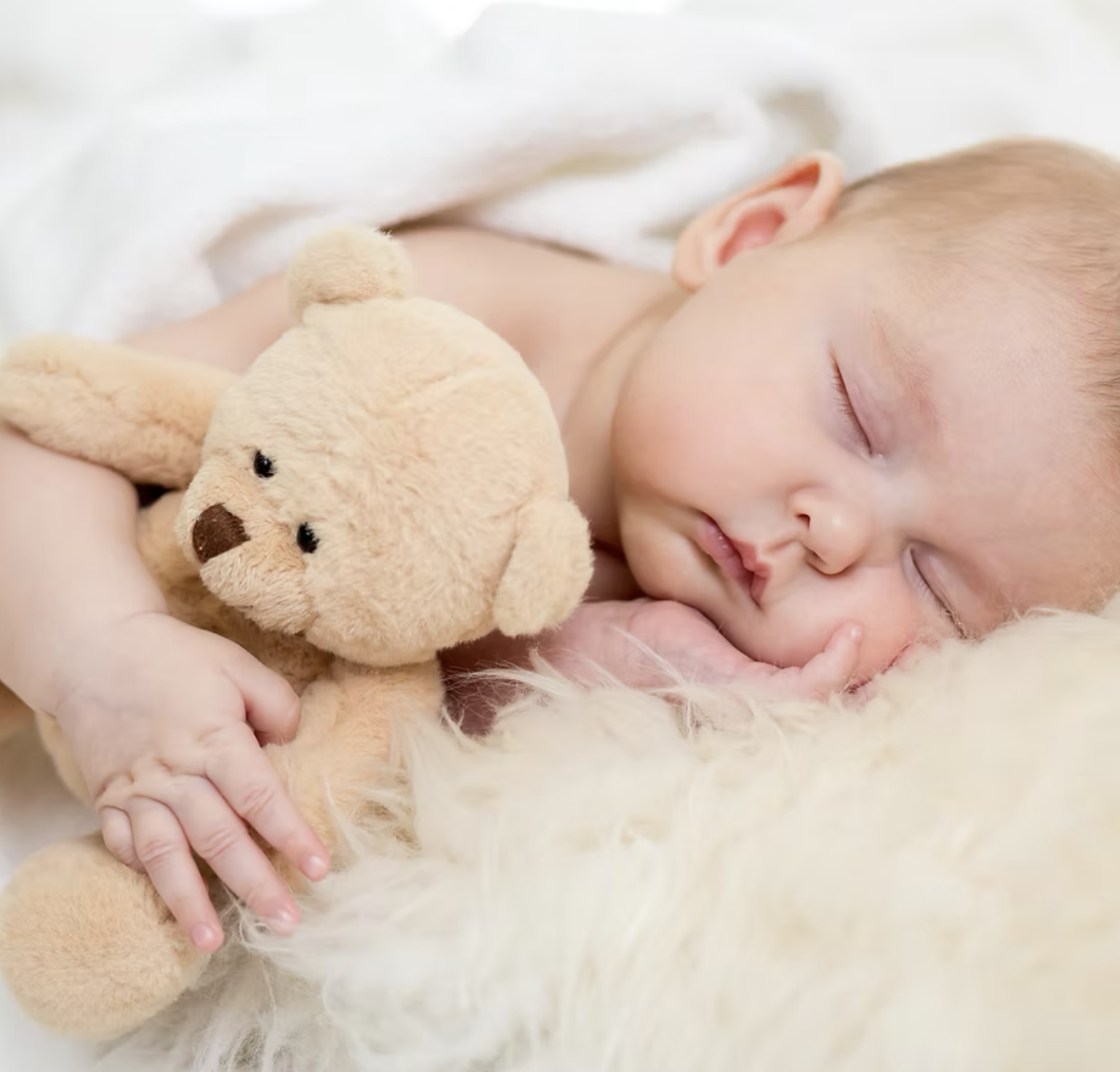 A sleeping baby lying on a soft surface, holding a plush teddy bear.
