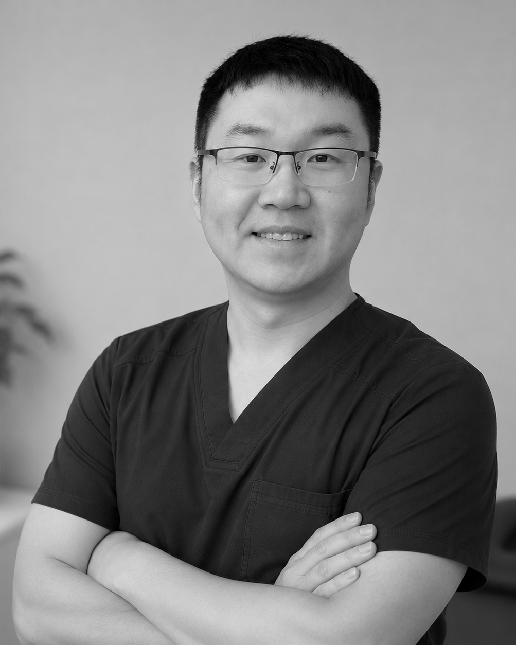 smiling, friendly Chinese man wearing massage scrubs with short clean-cut dark hair. wearing glasses with dark upper rim and clear lower frame.