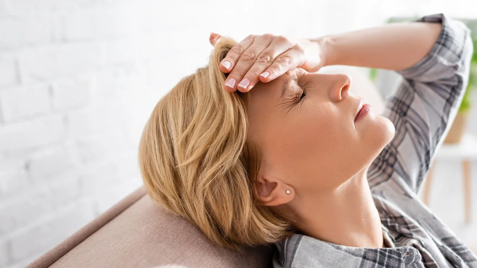 Woman experiencing headache, holding forehead with hand, eyes closed, relaxed posture