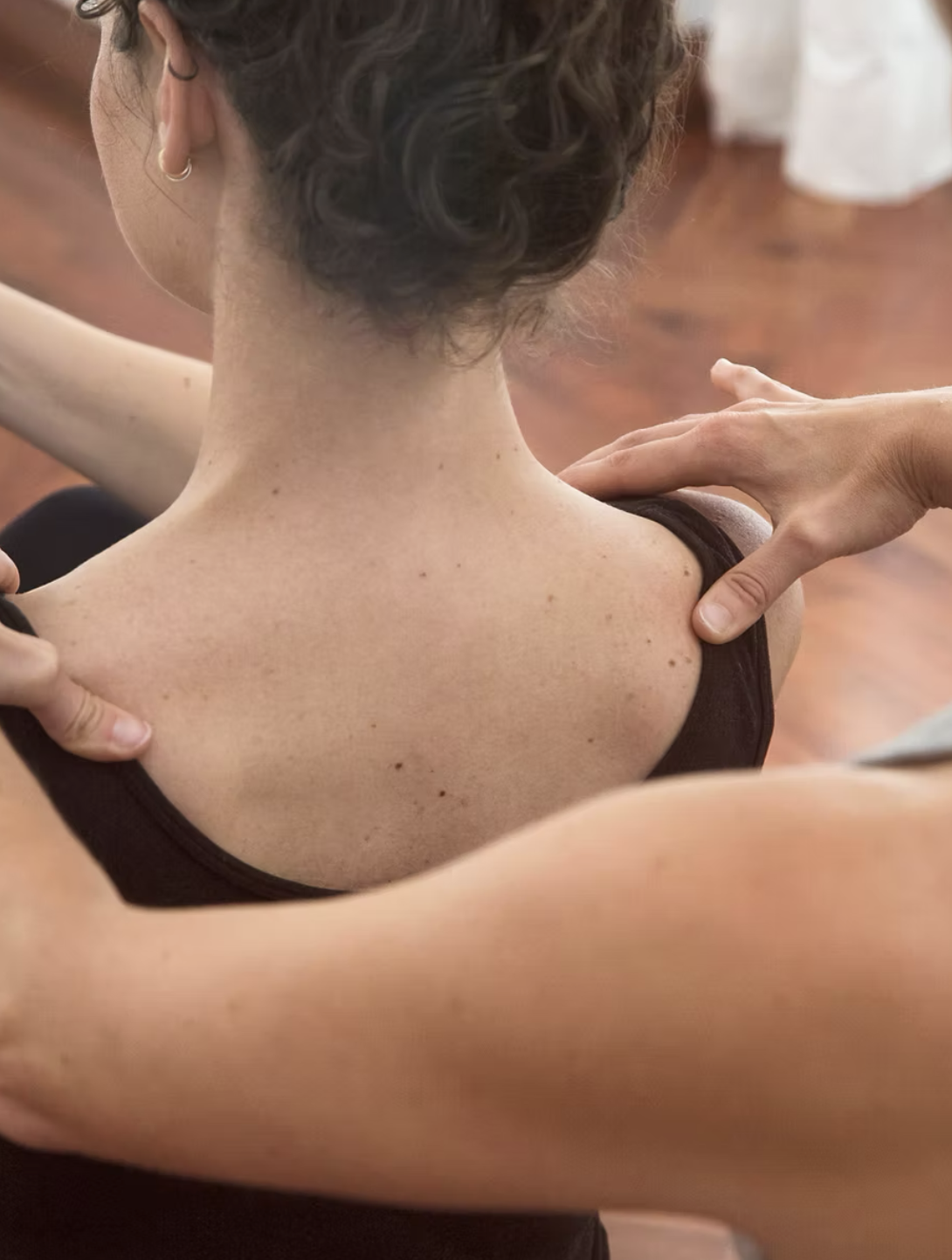 A person receiving a shoulder massage or physical therapy from another person in a room with wooden flooring.