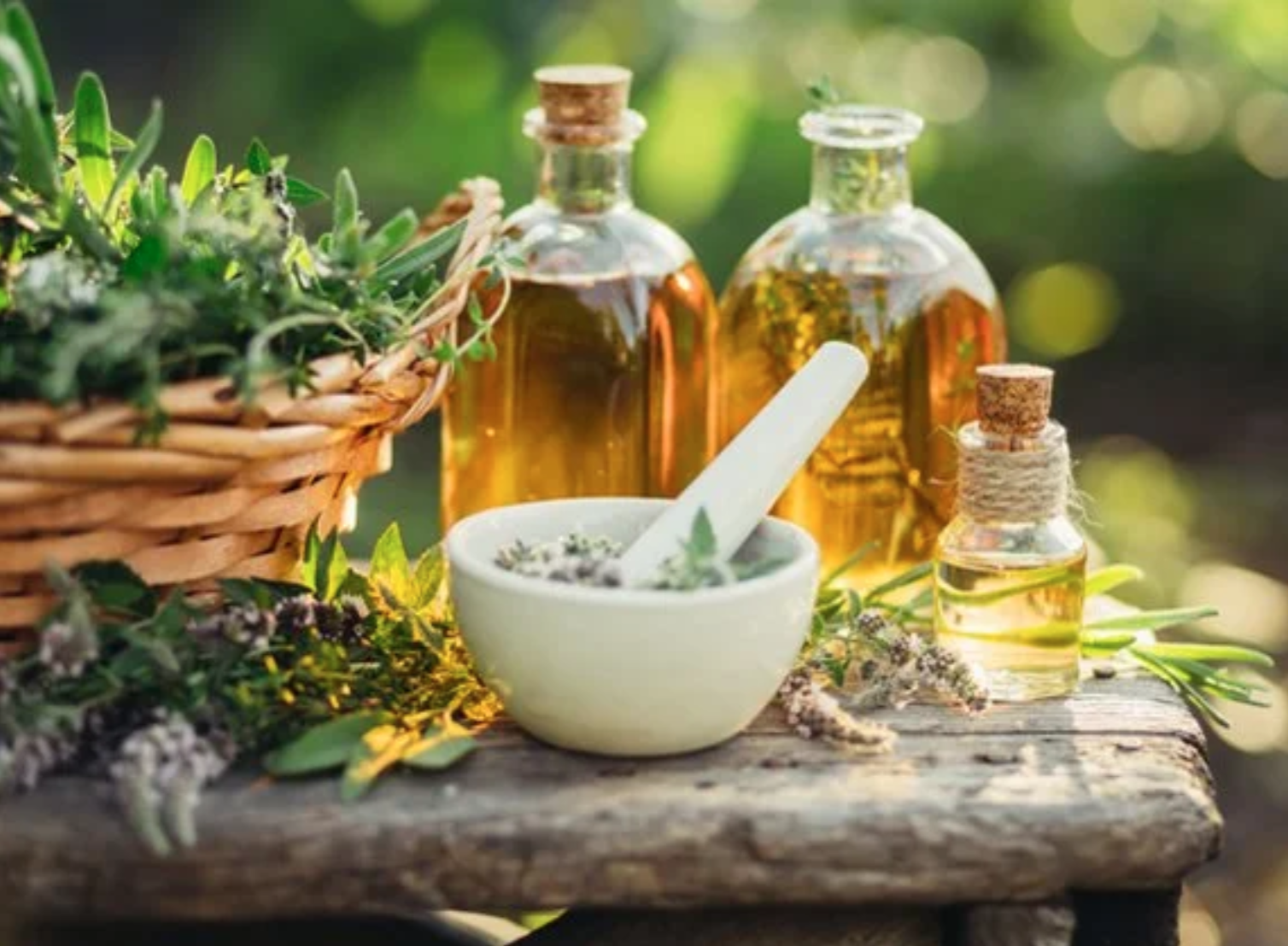 Herbal essential oils and dried herbs arranged on a rustic wooden surface outdoors.
