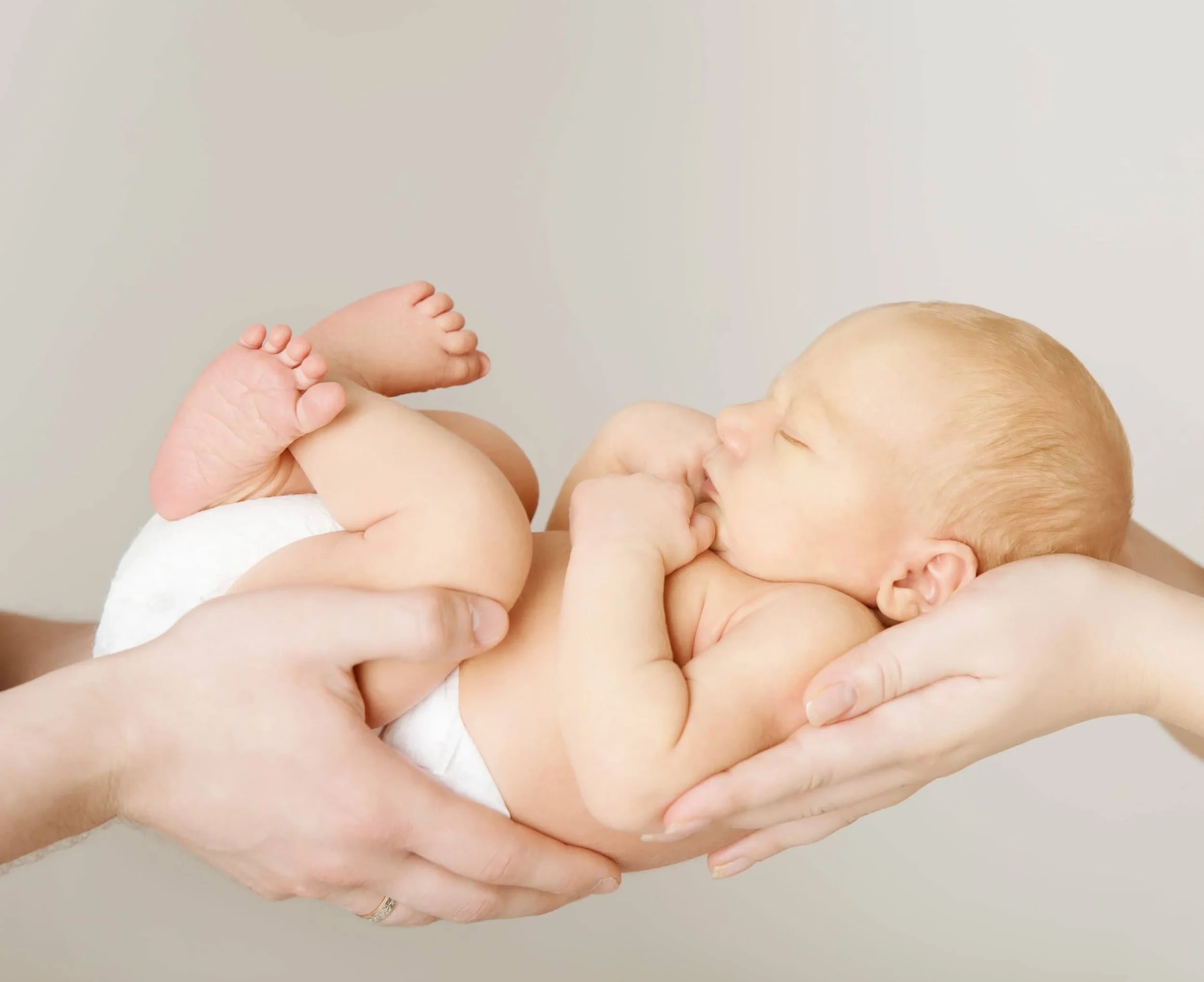 image of two sets of hands cupping a newborn baby in a diaper 