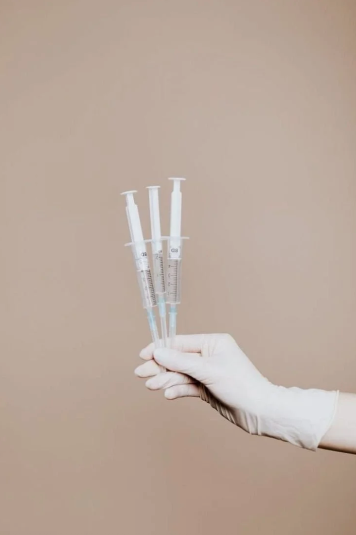 A gloved hand holding three syringes against a plain beige background.