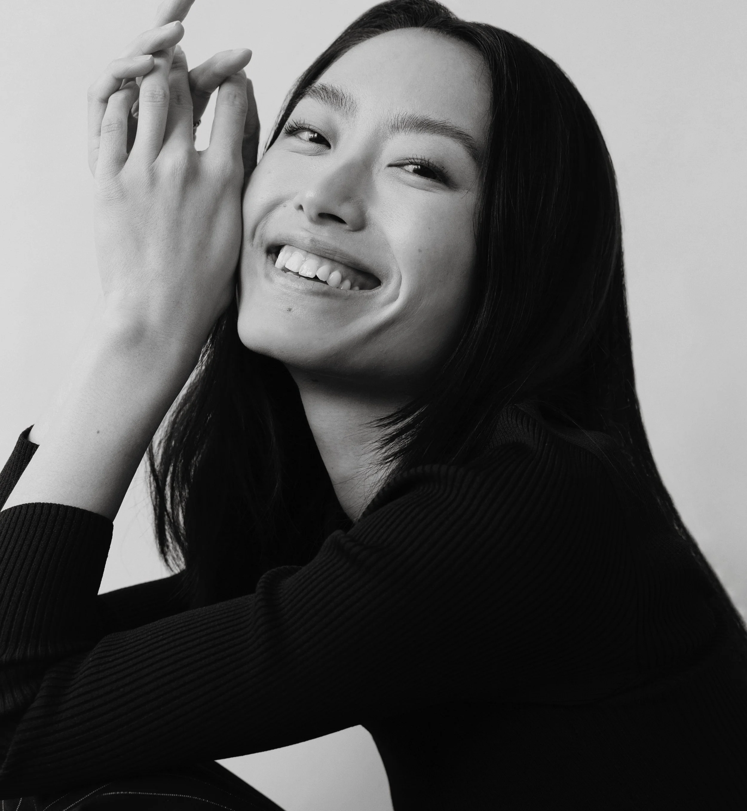 A woman smiling and playfully sticking out her tongue, with her hands near her face, wearing a black long-sleeve top.