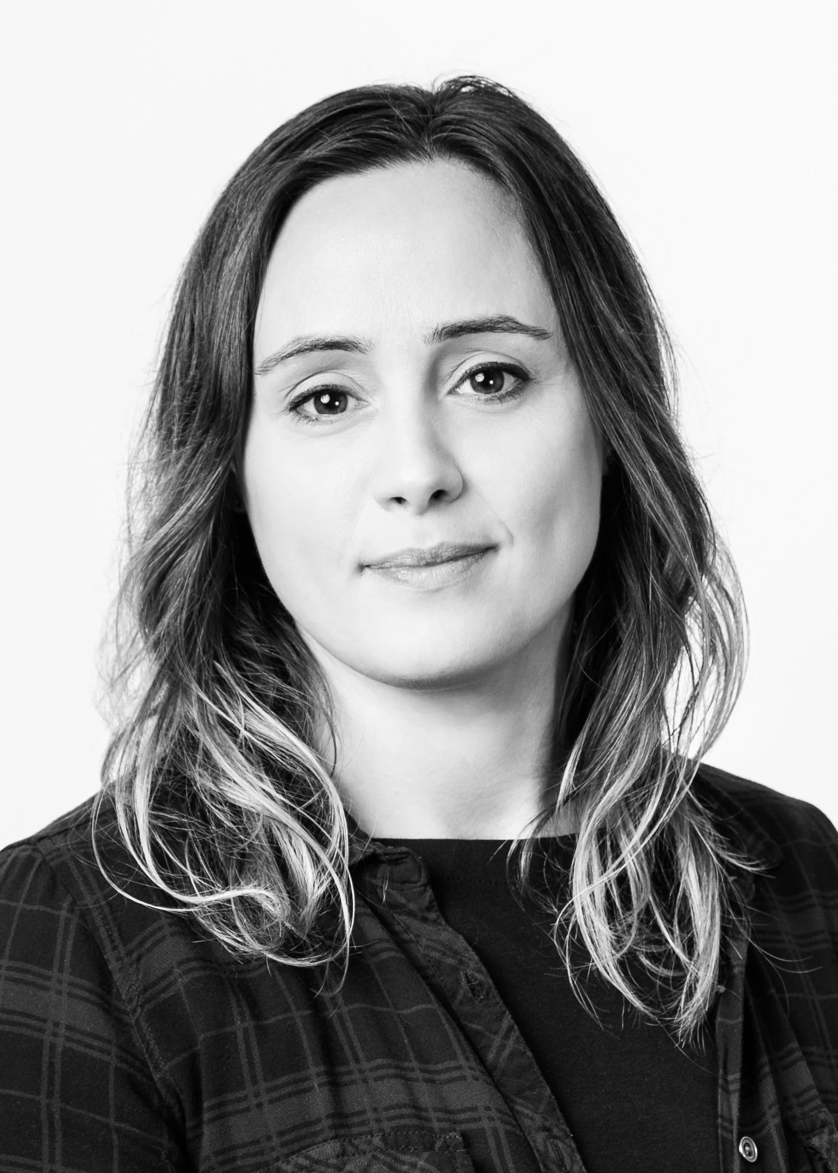 Black and white photo of a caucasian woman with long slightly wavy dark hair, highlighted at the ends wearing a plaid button shirt