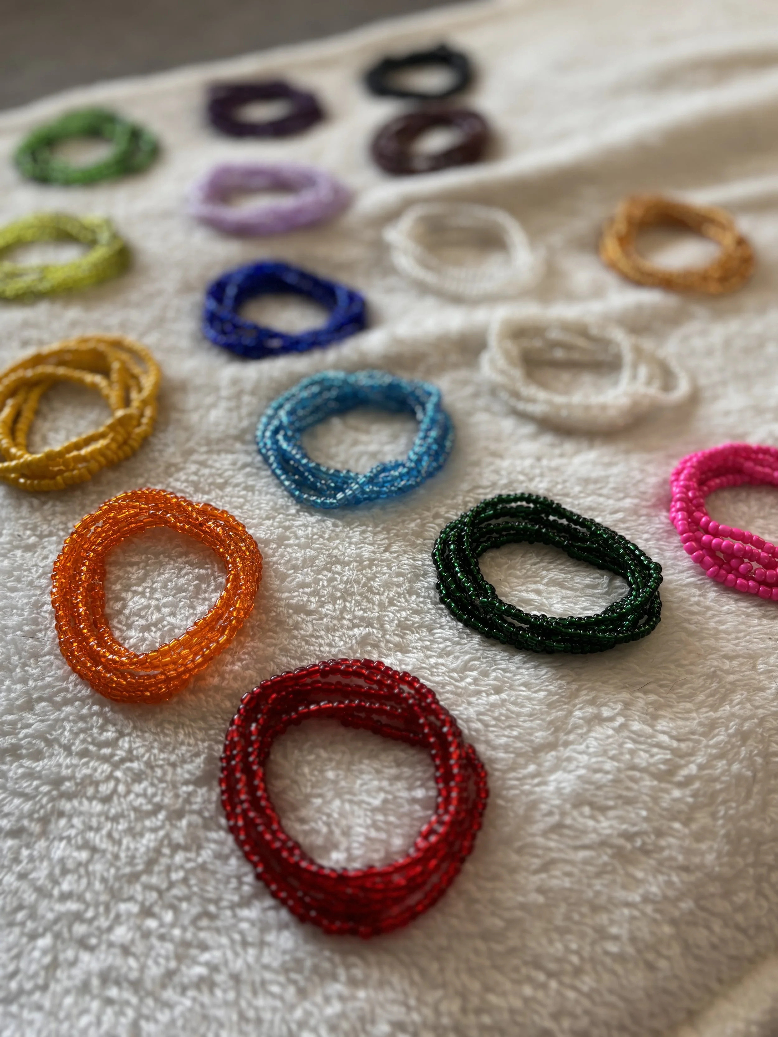 Colorful beaded bracelets arranged on a white textured surface in multiple rows.