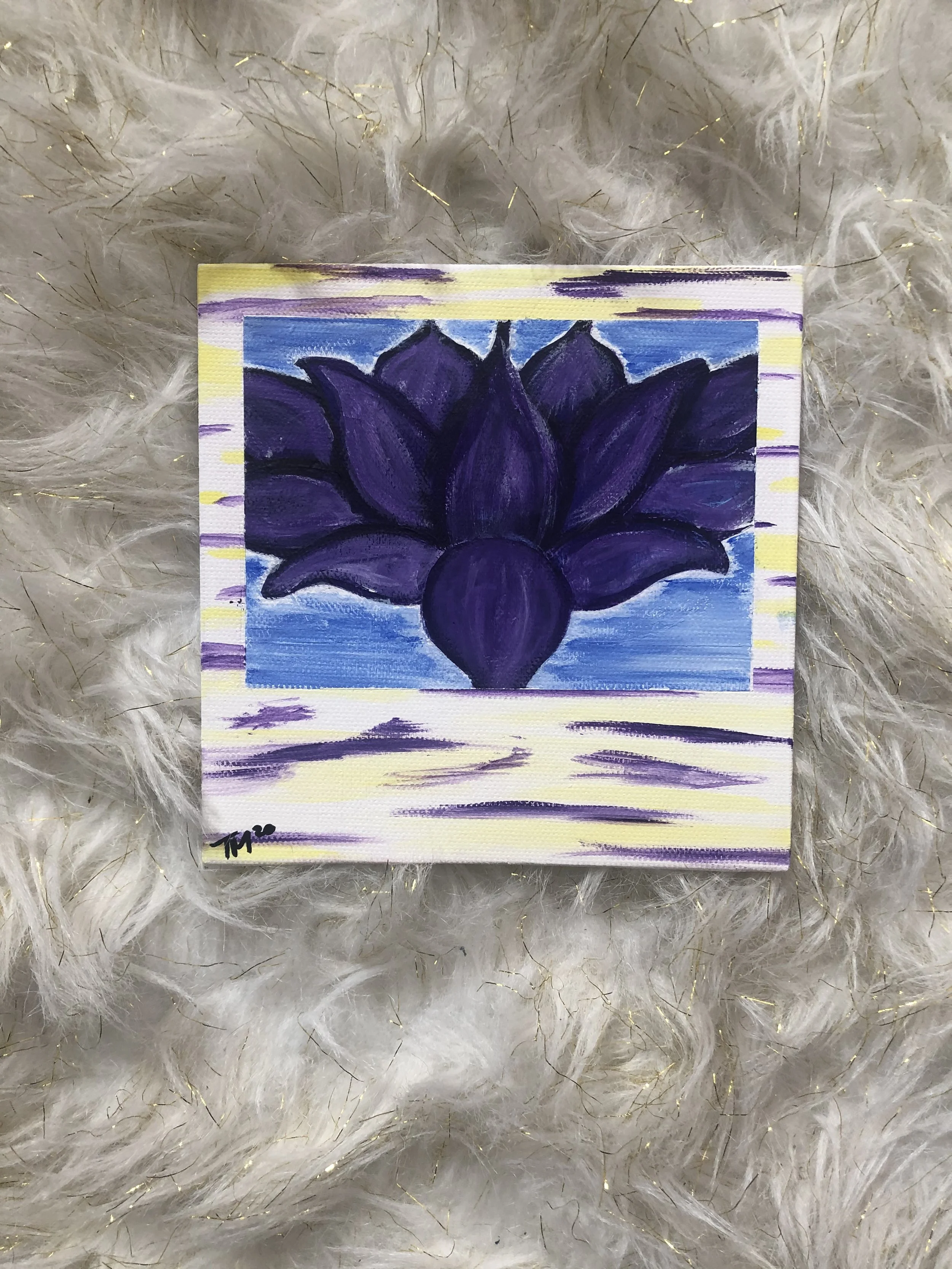 Miniature painting of a purple lotus flower on a small canvas, signed with initials 'M.P.' Boundary painted with light yellow and purple, background with shades of blue and purple, resting on a fluffy white and gold textured surface.