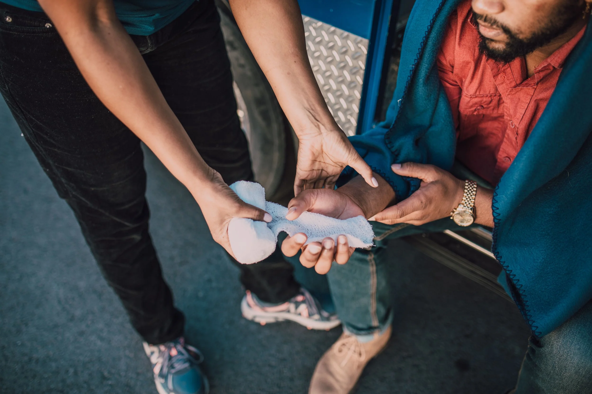 Person providing first aid by wrapping an injured arm during a trauma care response.