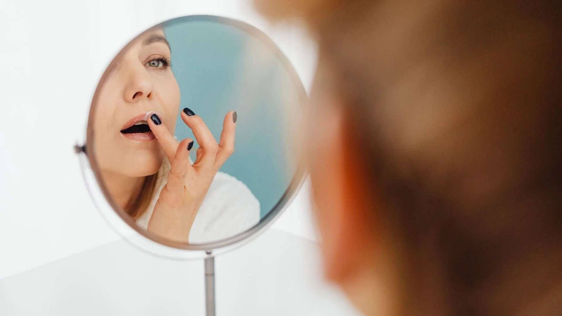 Woman applying lip balm at mirror — finding your skincare true love at Tina Rachelle Aesthetics Waite Park
