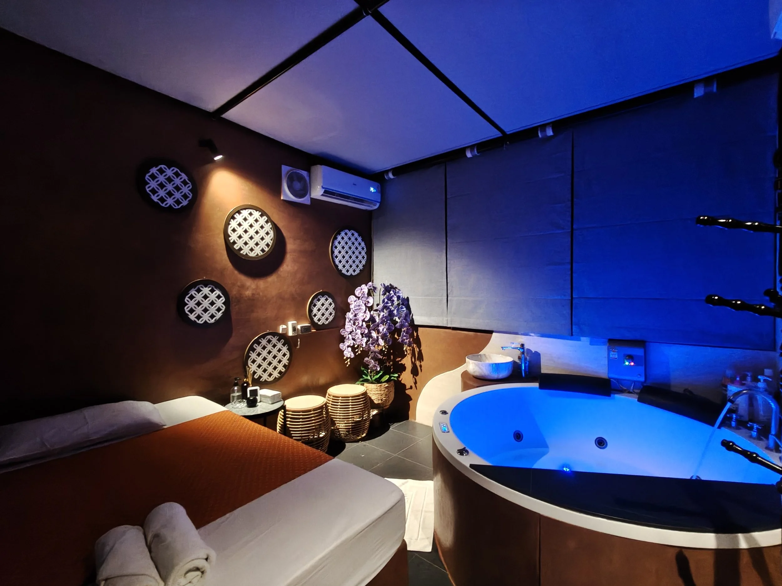 Indoor balcony with a bathtub, potted plants, blinds, and a view of tall buildings outside.