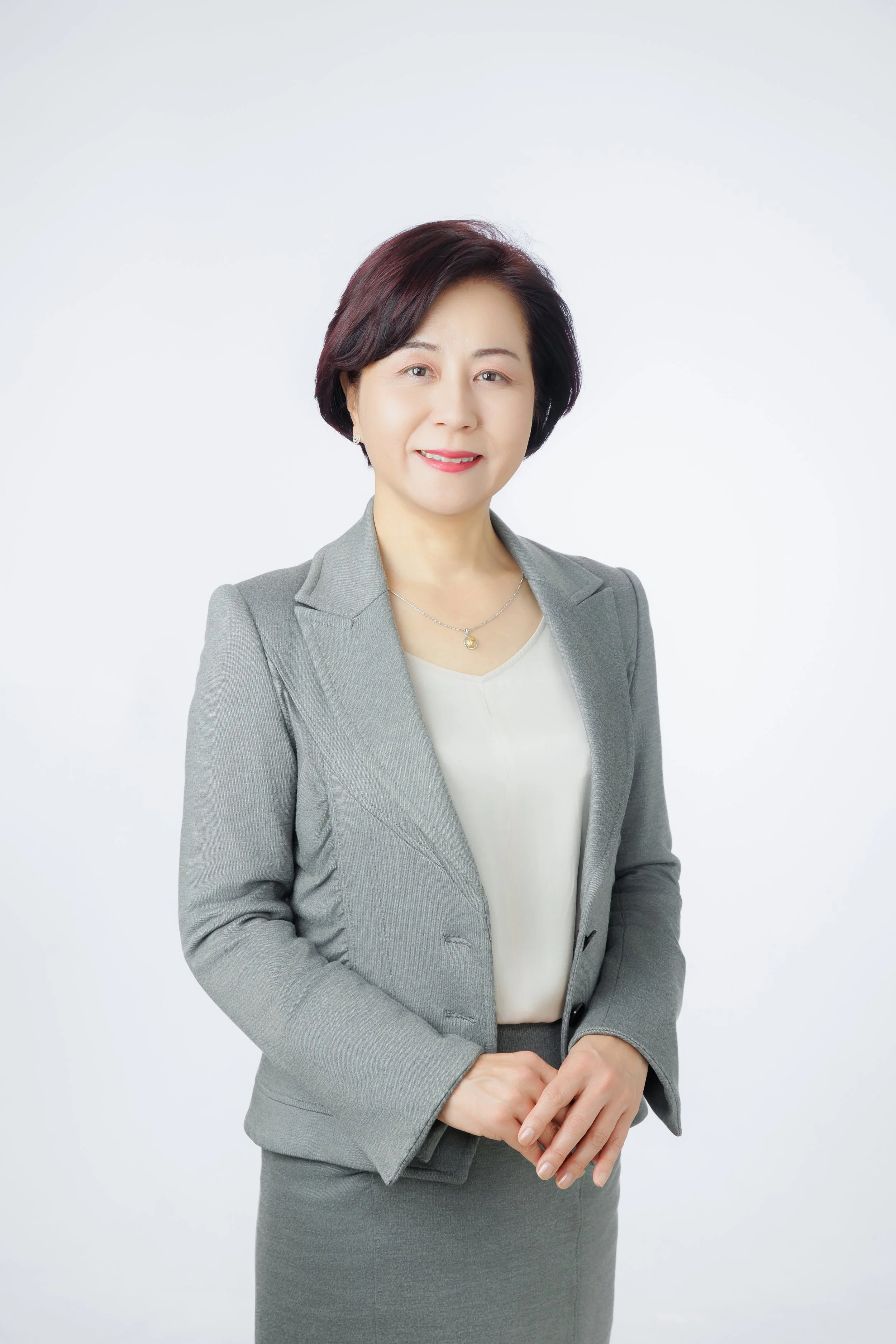 Professional woman in gray suit smiling, standing against a white background.