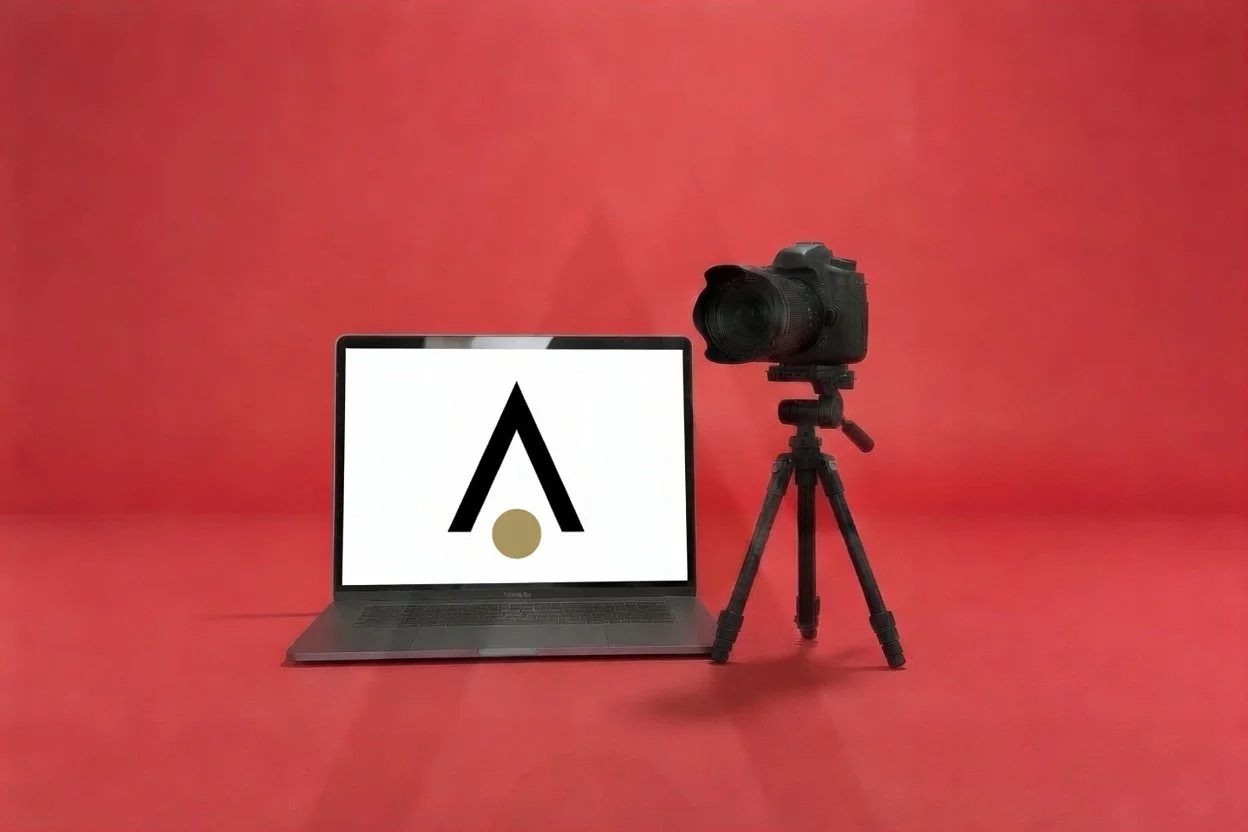 Laptop aberto com símbolo de Lambda na tela, ao lado uma câmera fotográfica em um tripé, tudo sobre fundo vermelho.