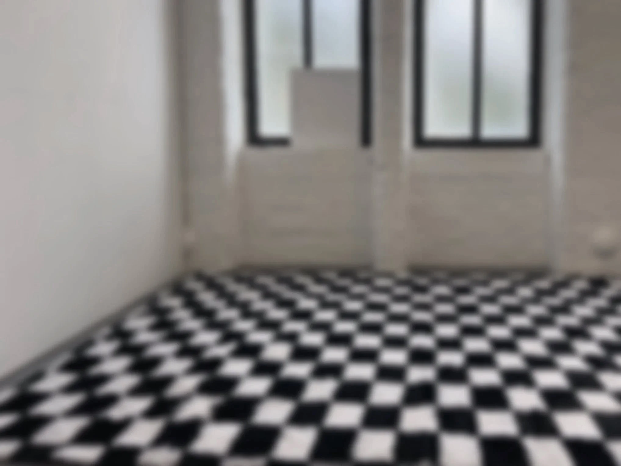 Empty room with black and white checkered floor tiles, large windows, and white walls.