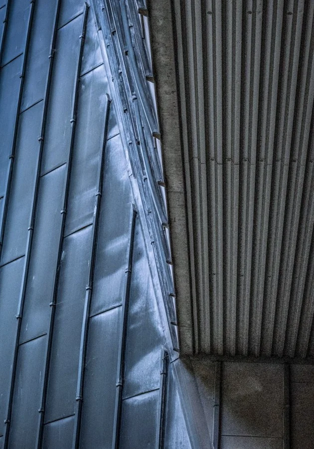 Abstract view of modern building surfaces showing converging lines, metal cladding and contrasting architectural textures.