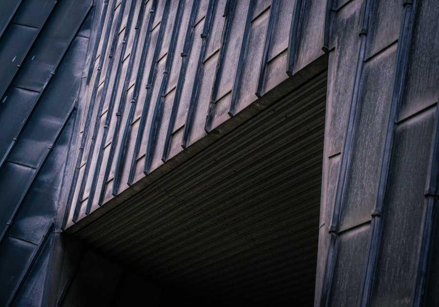 Abstract architectural detail showing intersecting metal-clad surfaces, strong lines and deep shadows on a modern building.