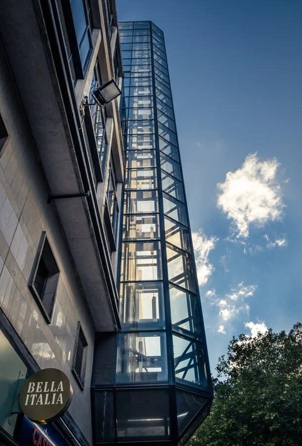 Lift Shaft Photo Walks Photography by Catherine Knee. Modern glass lift tower rising between contemporary city buildings in Birmingham's Paradise development.