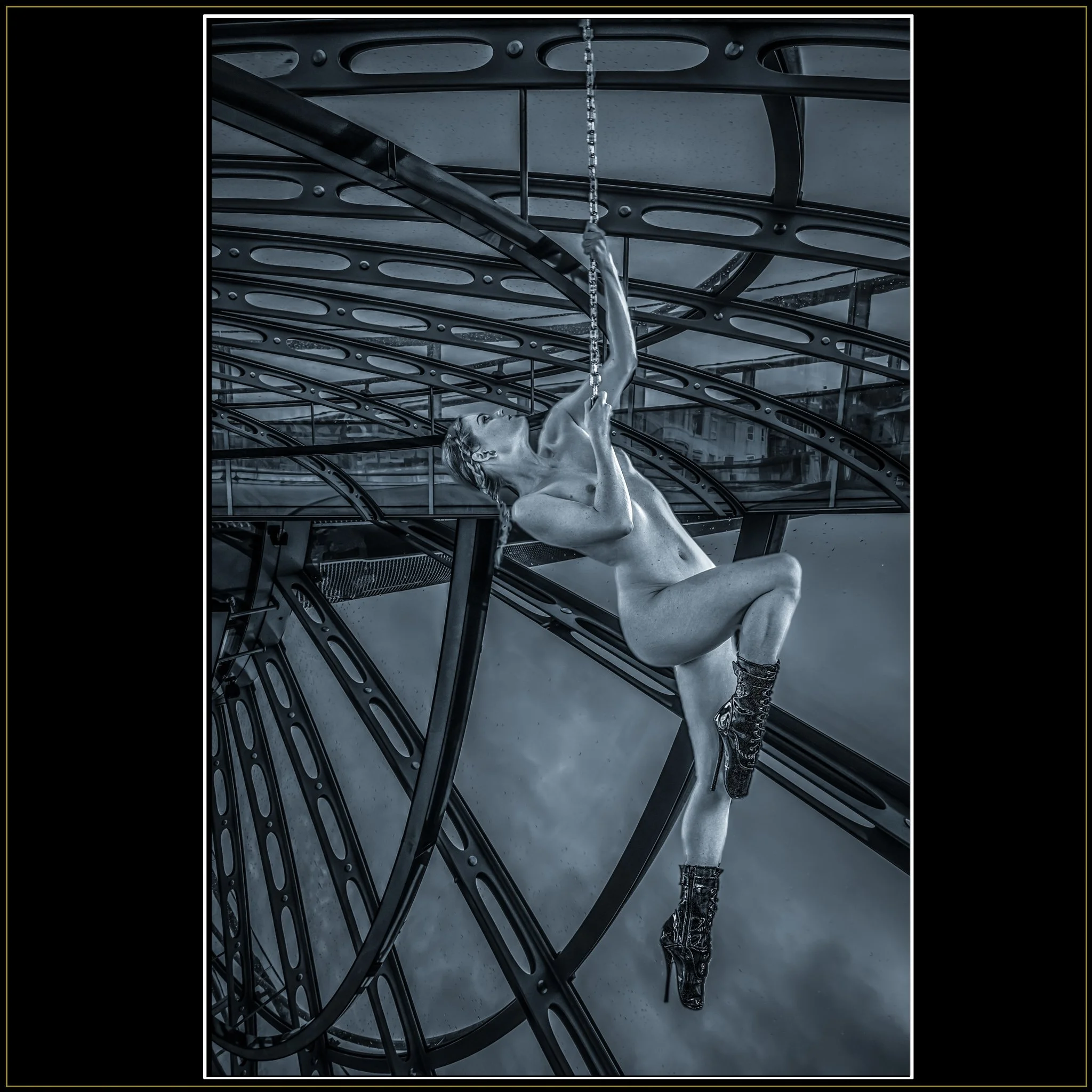 Aerial – Fine Art Nude Photography by Catherine Knee. A nude female figure with braided hair and high-heeled boots climbs a chain inside a dramatic metal and glass structure, her body arching upward against the geometric lines.
