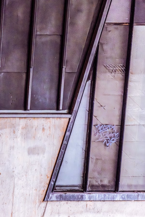 Abstract architectural detail featuring angled glass panels, metal framework and geometric shapes on a modern building.