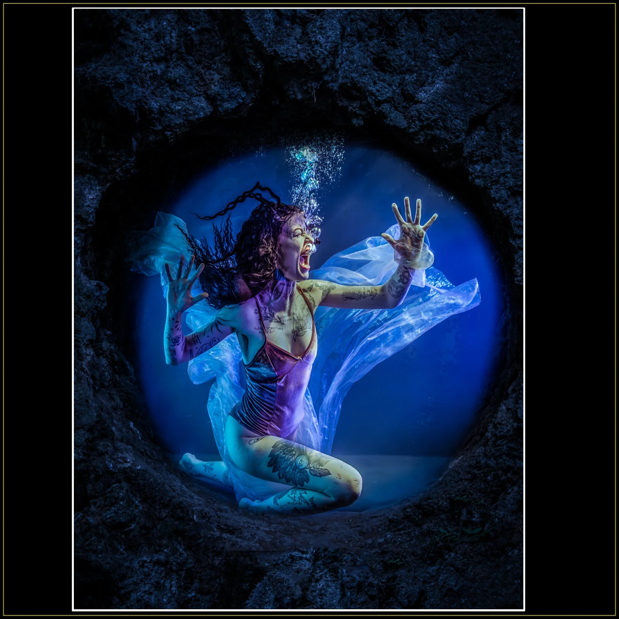 Let Me Out Of Here Dark-Art Photography by Catherine Knee. Dramatic underwater image of woman screaming in blue-lit tank embedded in rock with flowing translucent fabric and rising air bubbles.