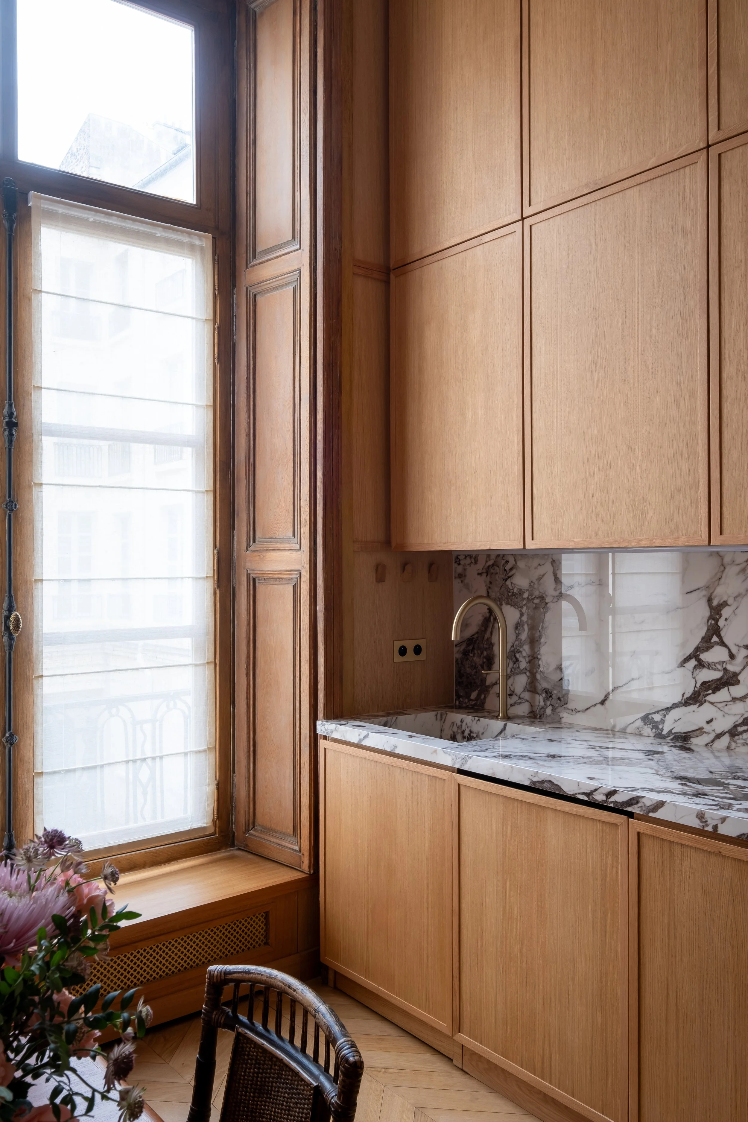 Détail robinetterie laiton brossé, crédence et plan de travail marbre veiné, lumière naturelle, fenêtre haussmannienne d'origine rénovée, Paris.