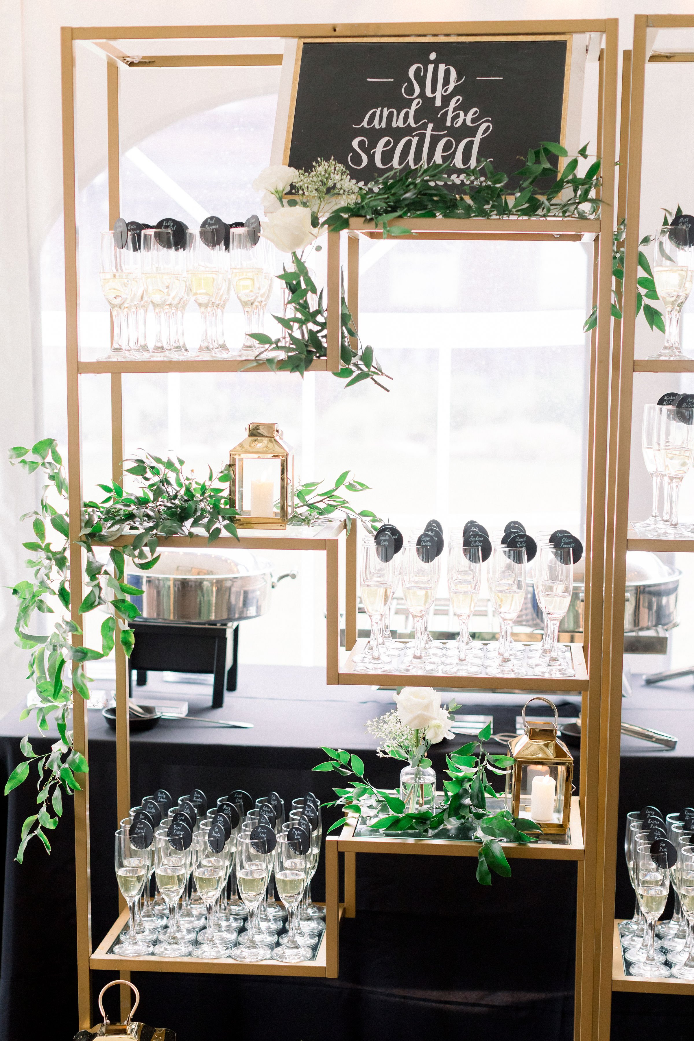 Golden bookcase with champagne glasses and custom escort cards and smilax vine