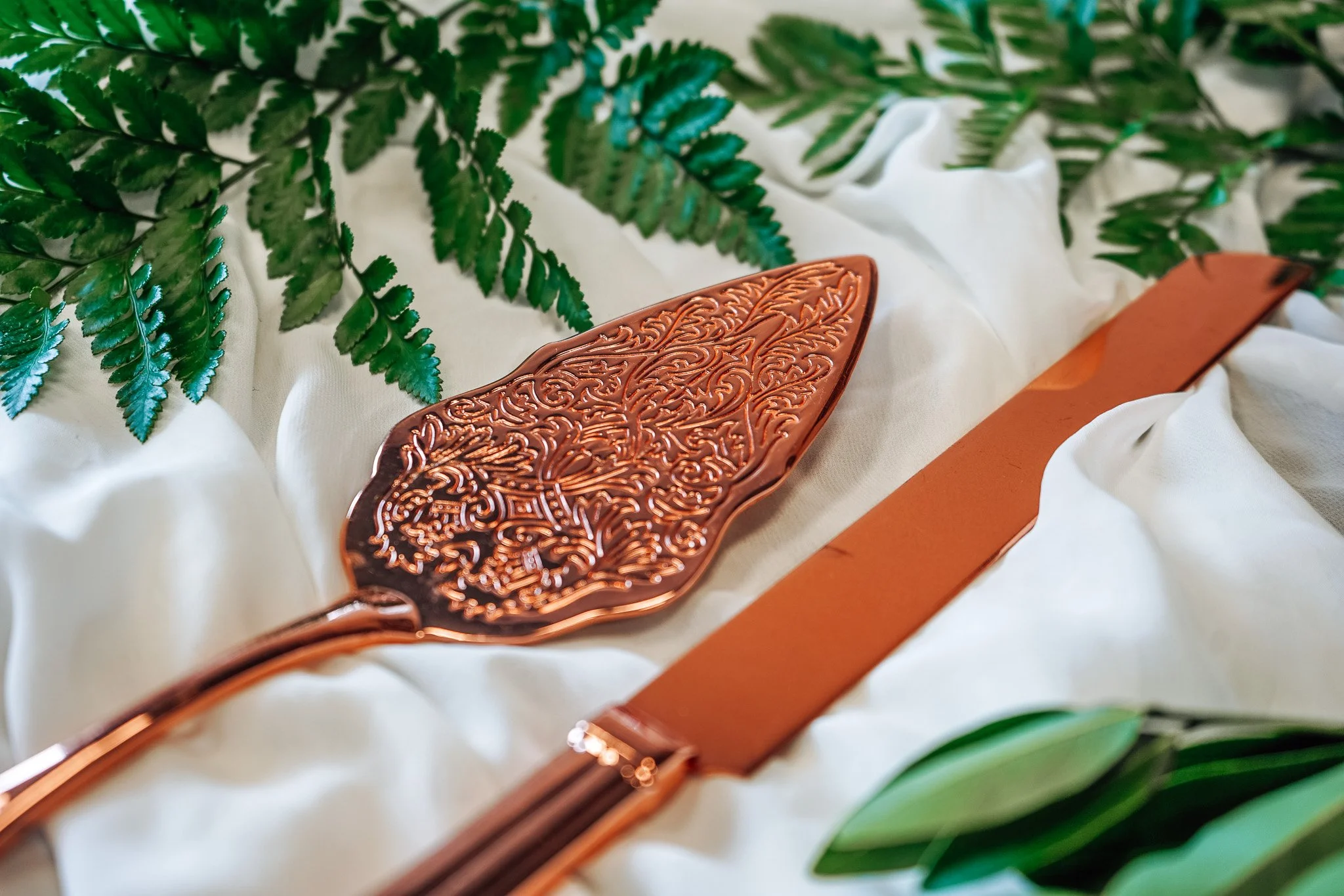 rose fold cake cutting decor on a white table cloth with greenery adorning the background