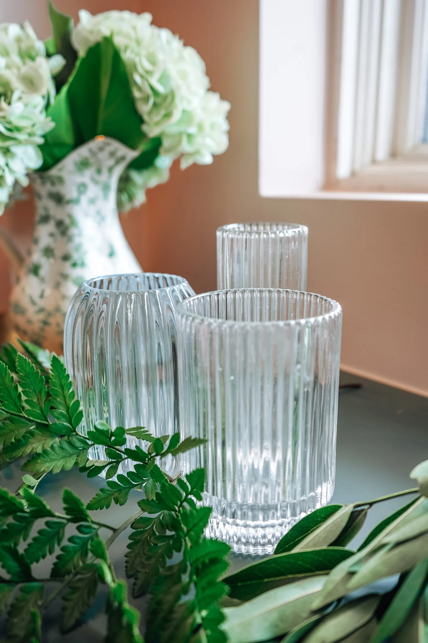A trio of clear pleated candle holders with a floral vase in the background