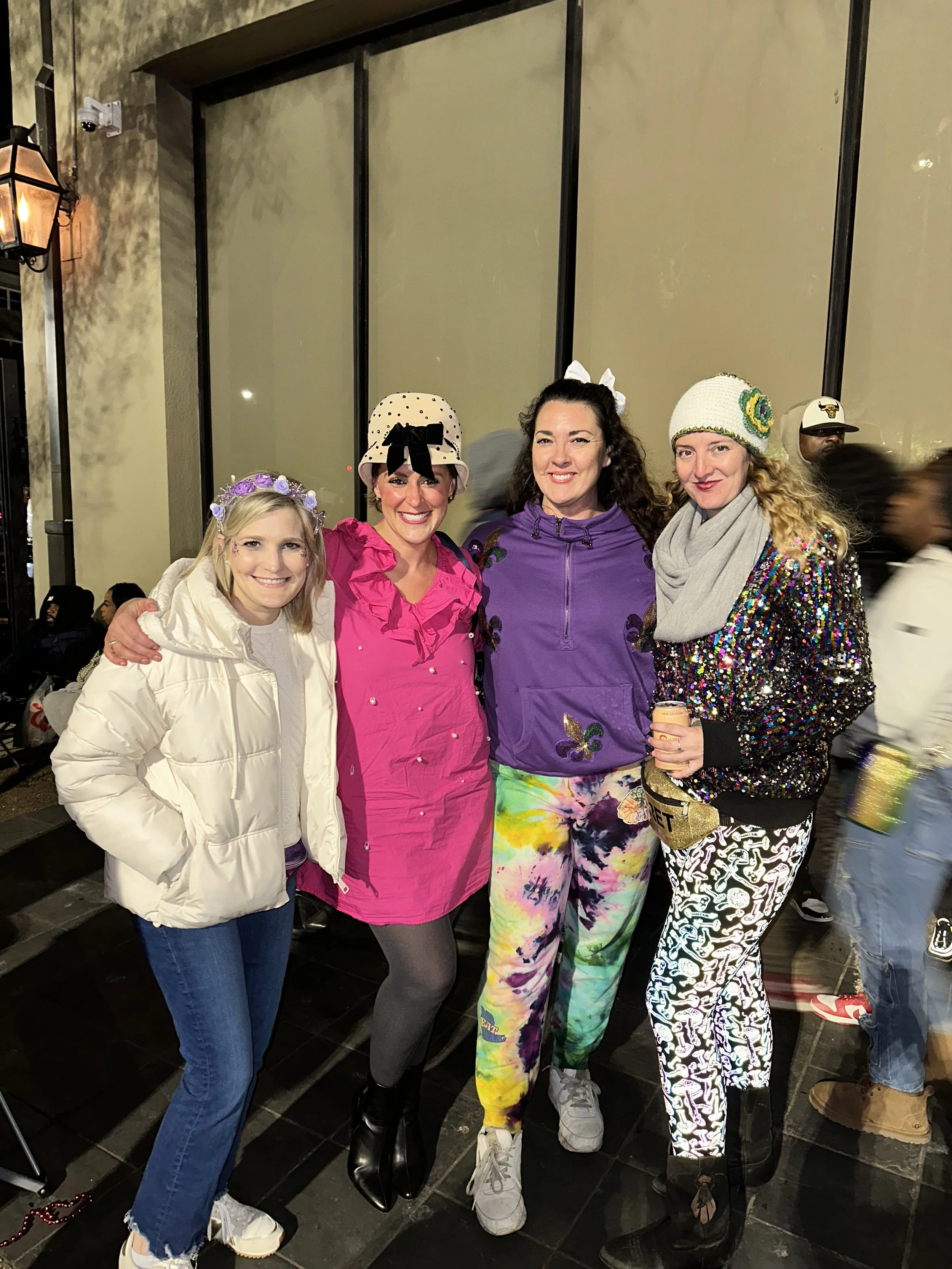 Four women standing together outside at night, dressed in colorful, festive clothing.