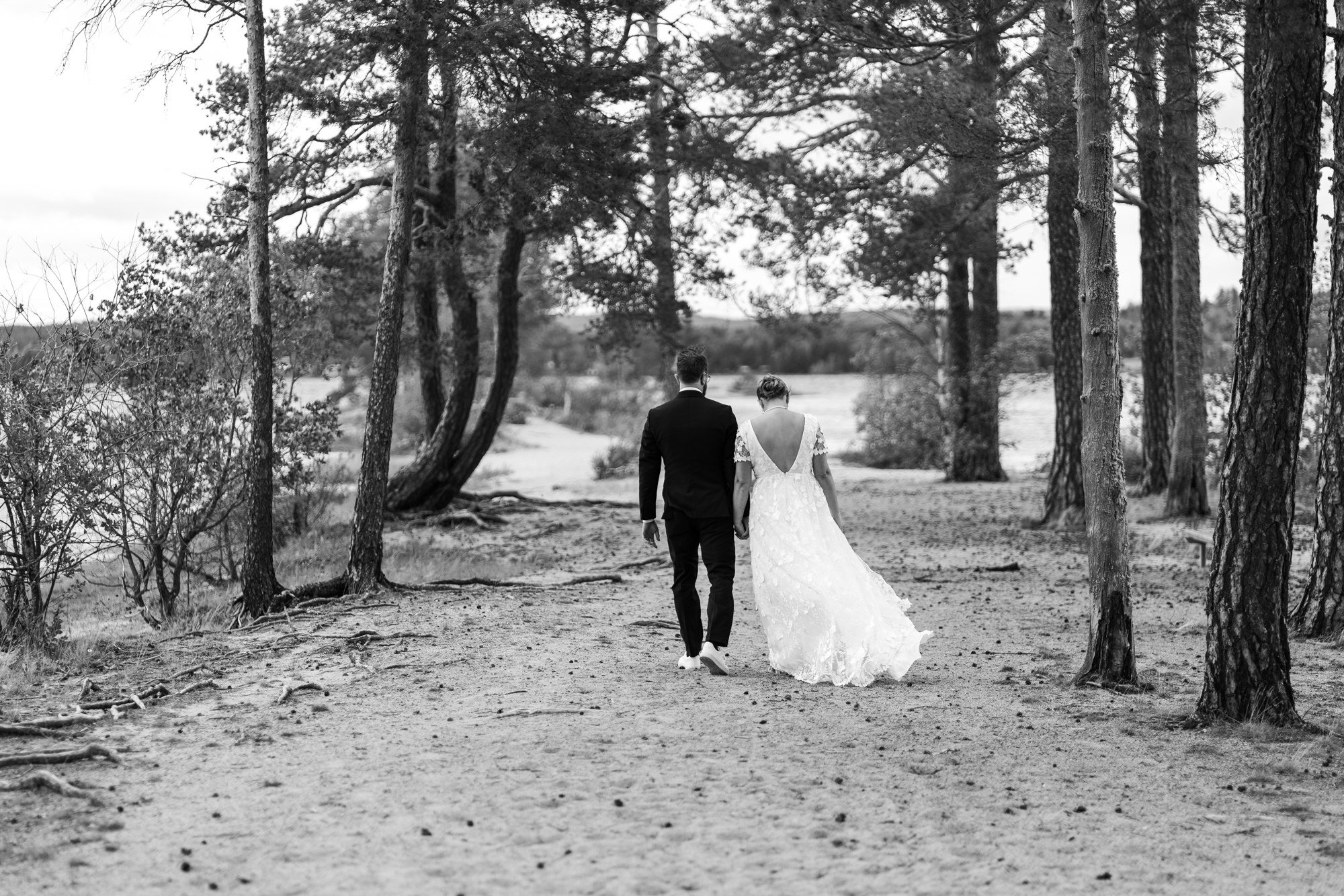 Brudpar går tillsammans längs en stig bland träd.