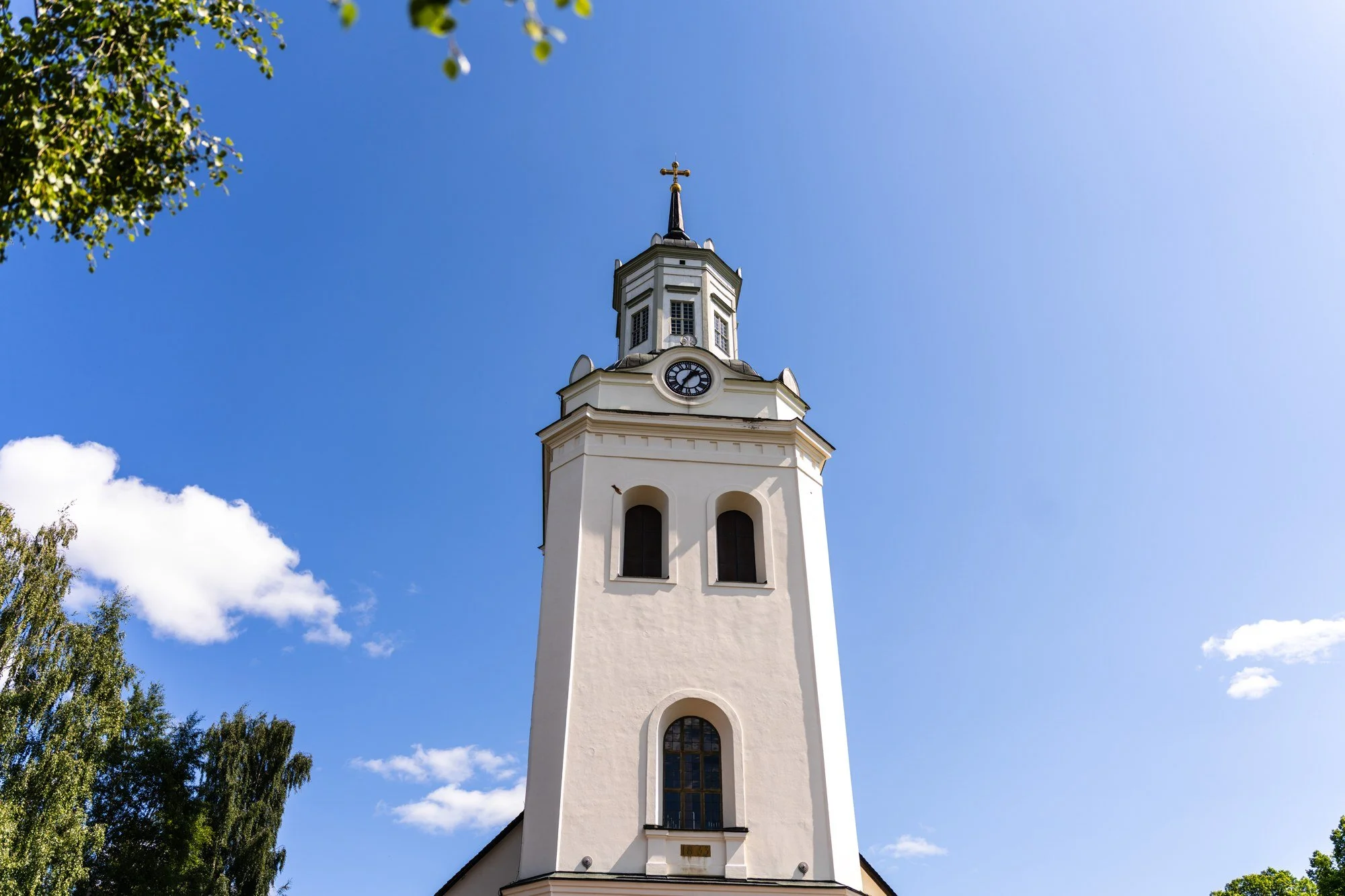 Vitt kyrktorn mot en blå sommarhimmel.