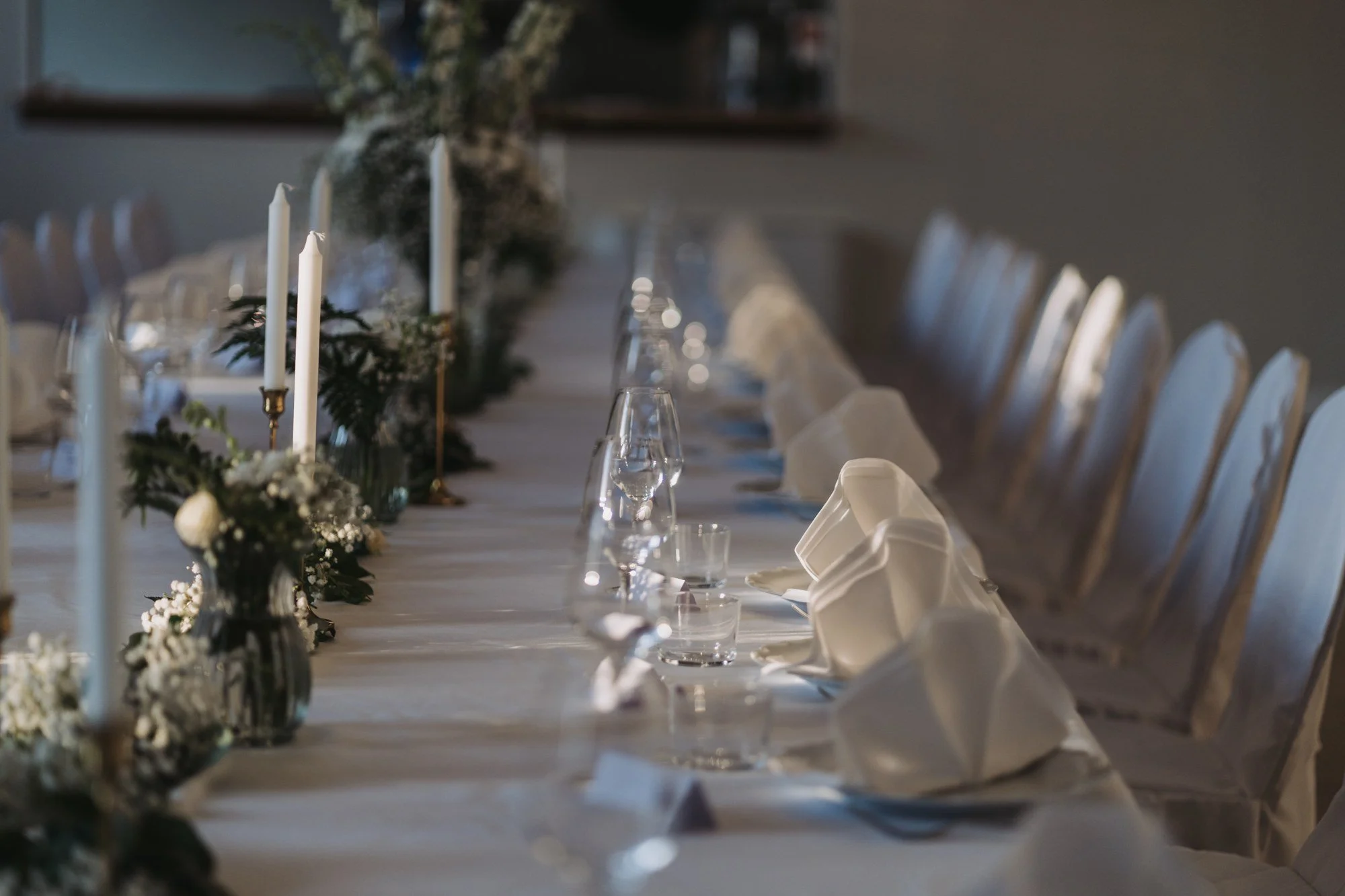 Långbord dukat med vita servetter, glas och blommor.