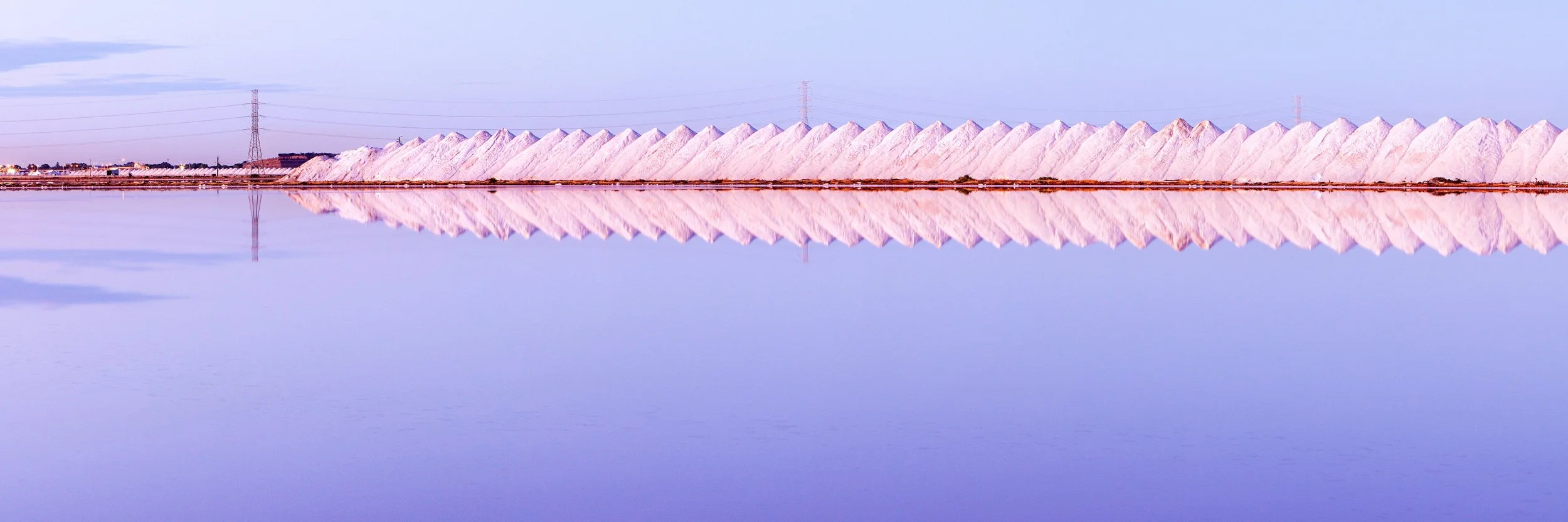 Minimalist landscape of Port Adelaide salt pans in South Australia, with pale pink salt mounds reflected in still water.