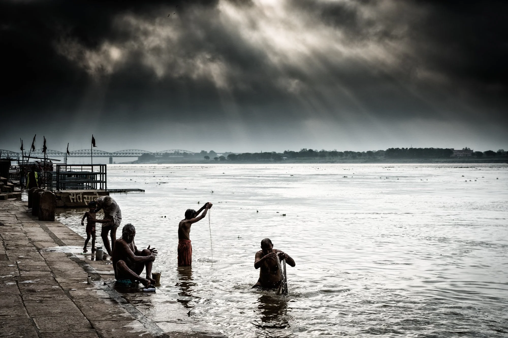 Dramatic black and white view of people bathing in the Ganges River at Varanasi ghats under dark monsoon clouds, India.