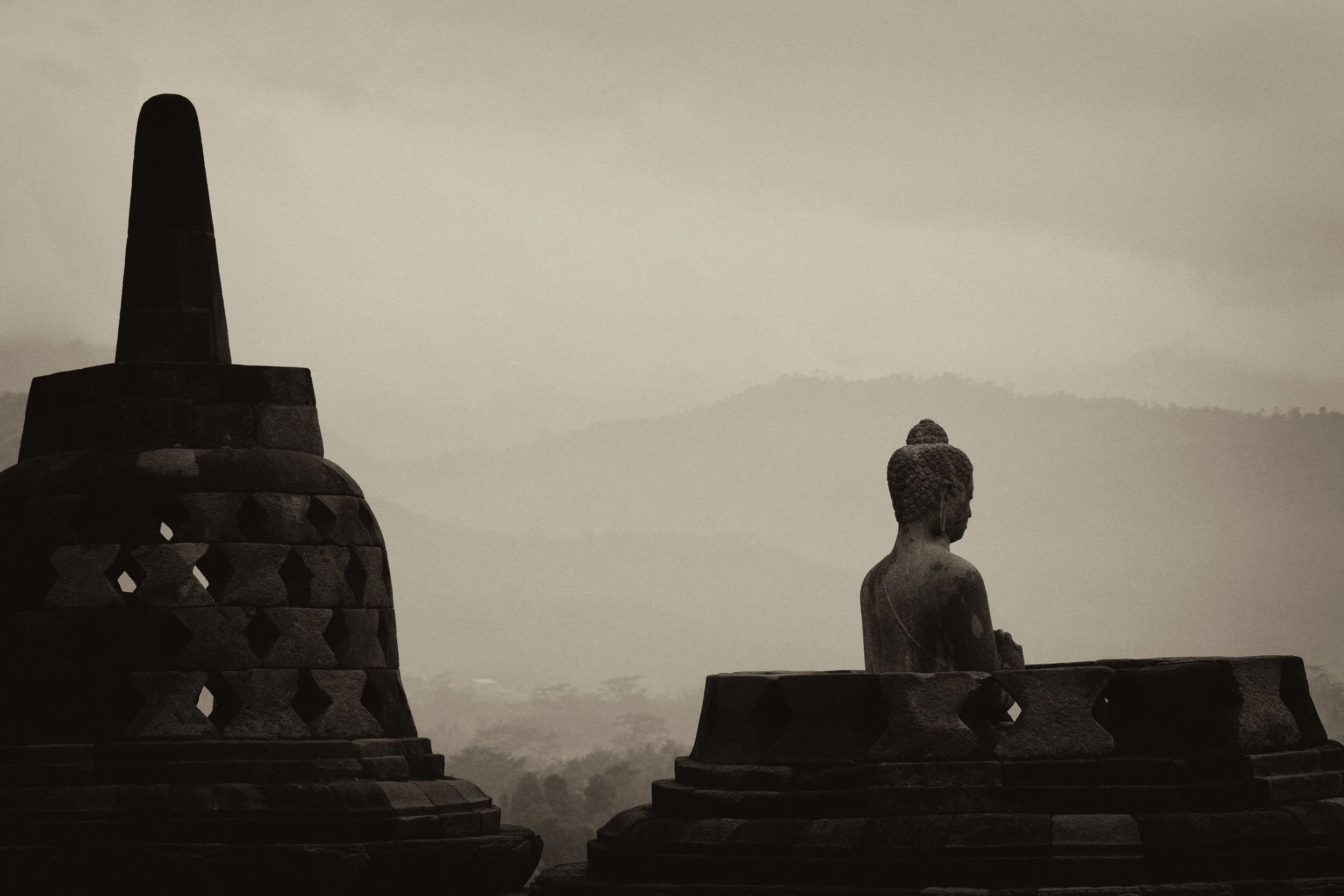 Monochrome Buddha statue and stupa silhouette overlooking hazy mountains in Myanmar.